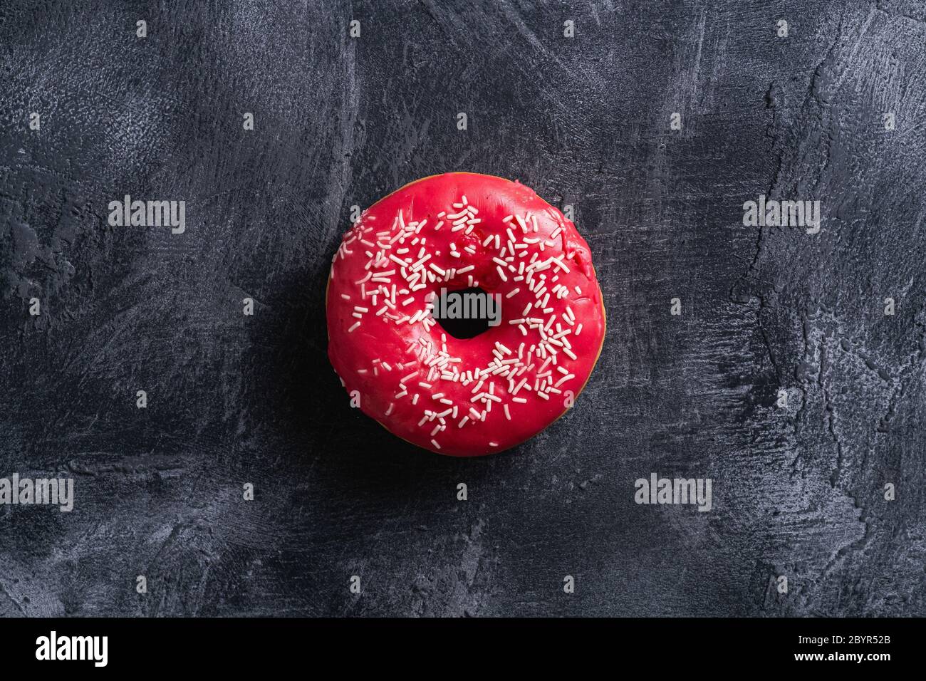 Ciambella rosa con spruzzi, dessert con caramelle su fondo ruvido in cemento, vista dall'alto Foto Stock