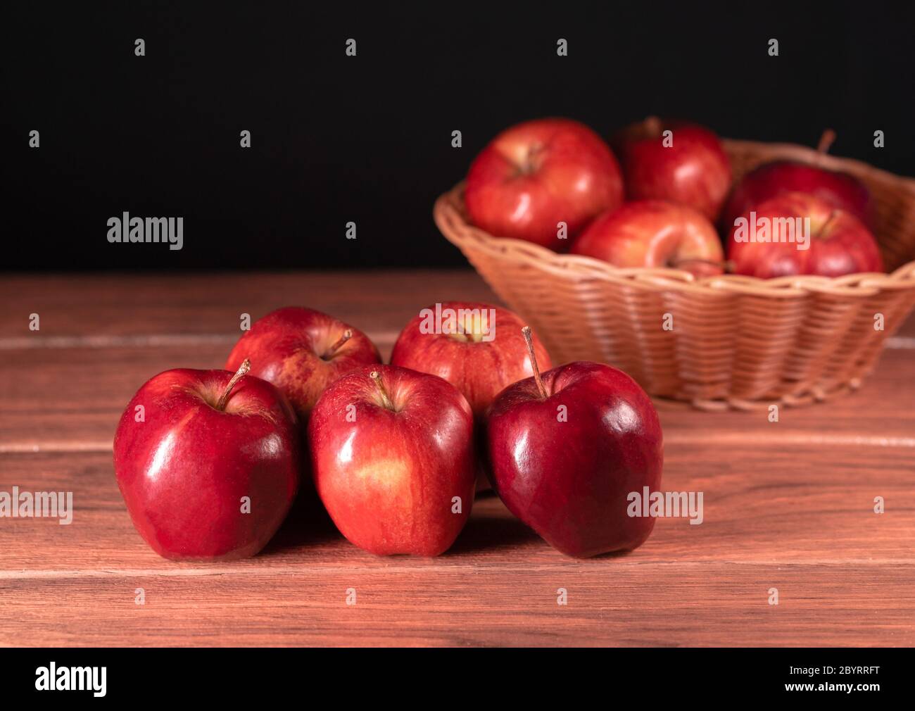 Molte mele rosse fresche con cesto marrone con più mele in primo piano sullo sfondo Foto Stock