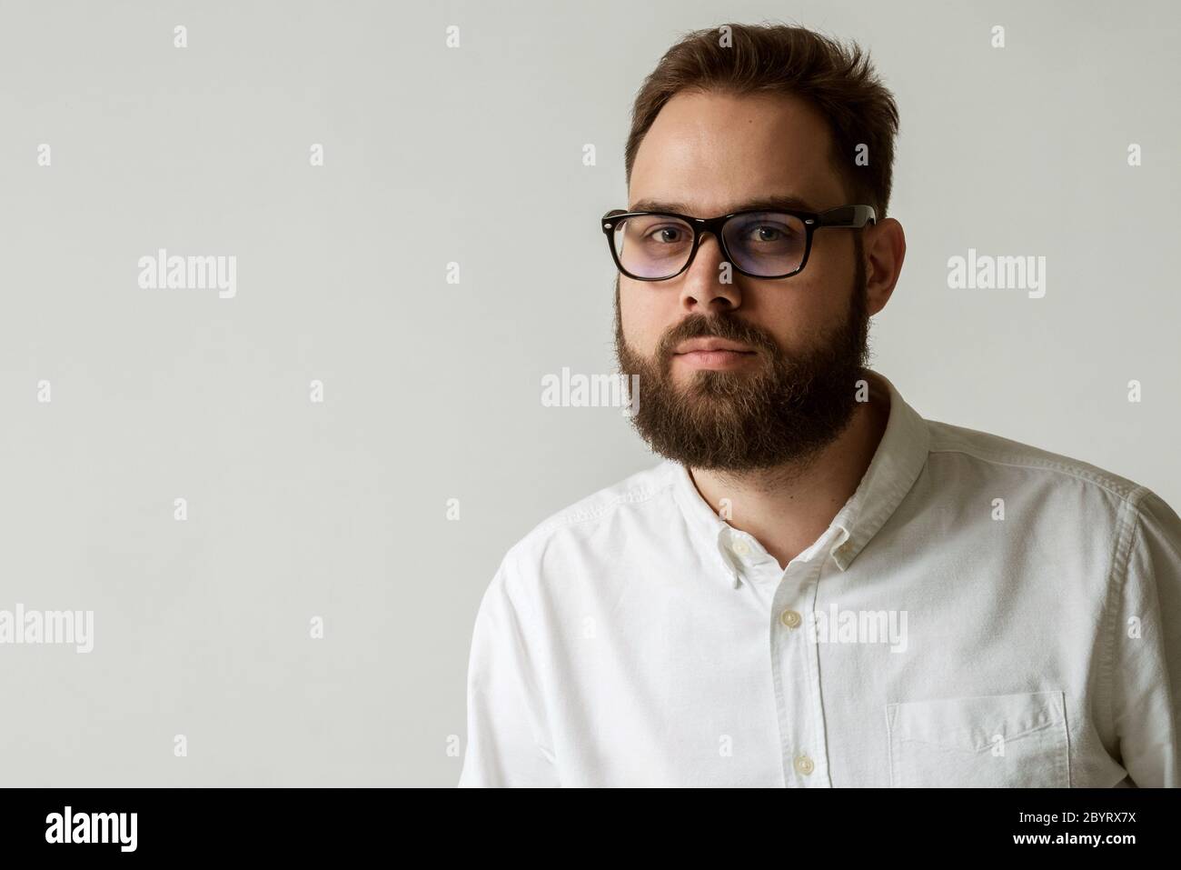 Testa e spalle ritratto di bell'uomo con barba isolata su sfondo bianco con spazio per la copia. Modello con camicia bianca e occhiali Foto Stock