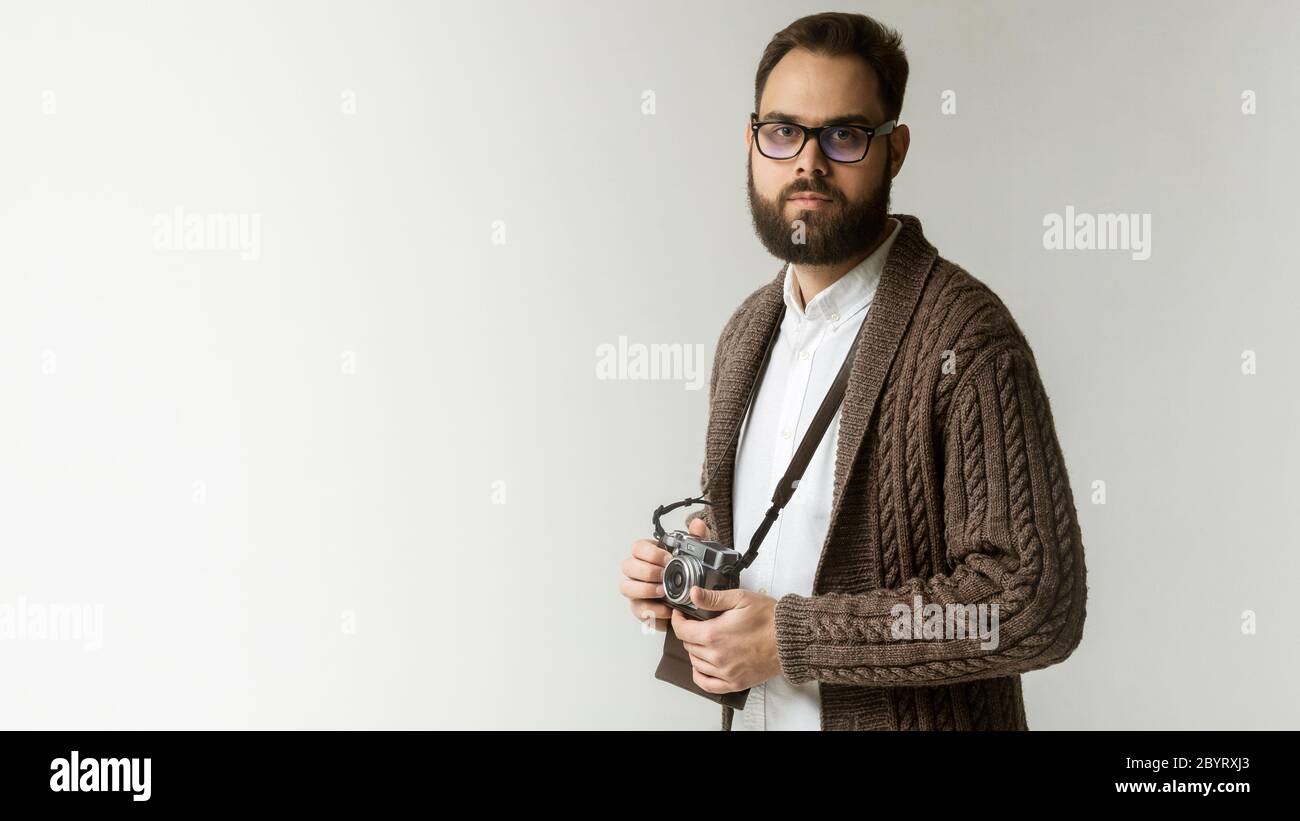Fotografo esperto con fotocamera su una cinghia isolata su sfondo bianco. Modello con pullover marrone caldo e ha un bel nero Foto Stock