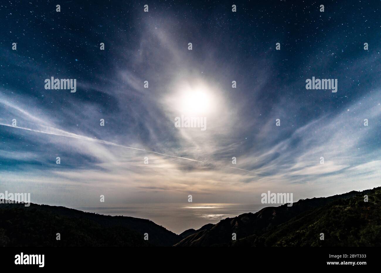 Cielo stellato notturno californiano illuminato dalla luna piena sull'oceano dietro le nuvole Foto Stock