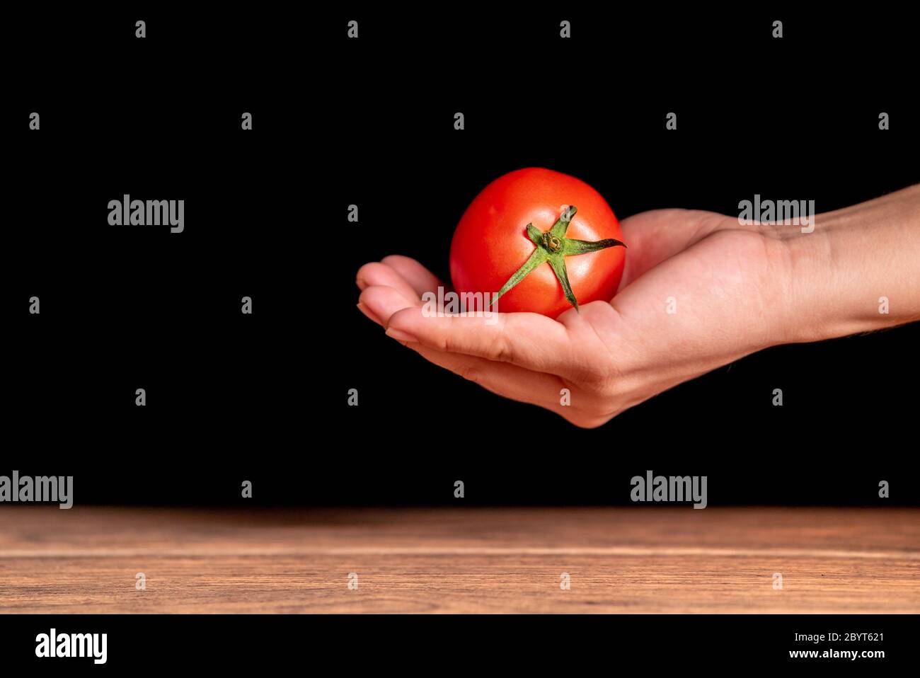 Pomodoro maturo con il suo gambo verde sulla mano di persona nell'aria con sfondo nero Foto Stock