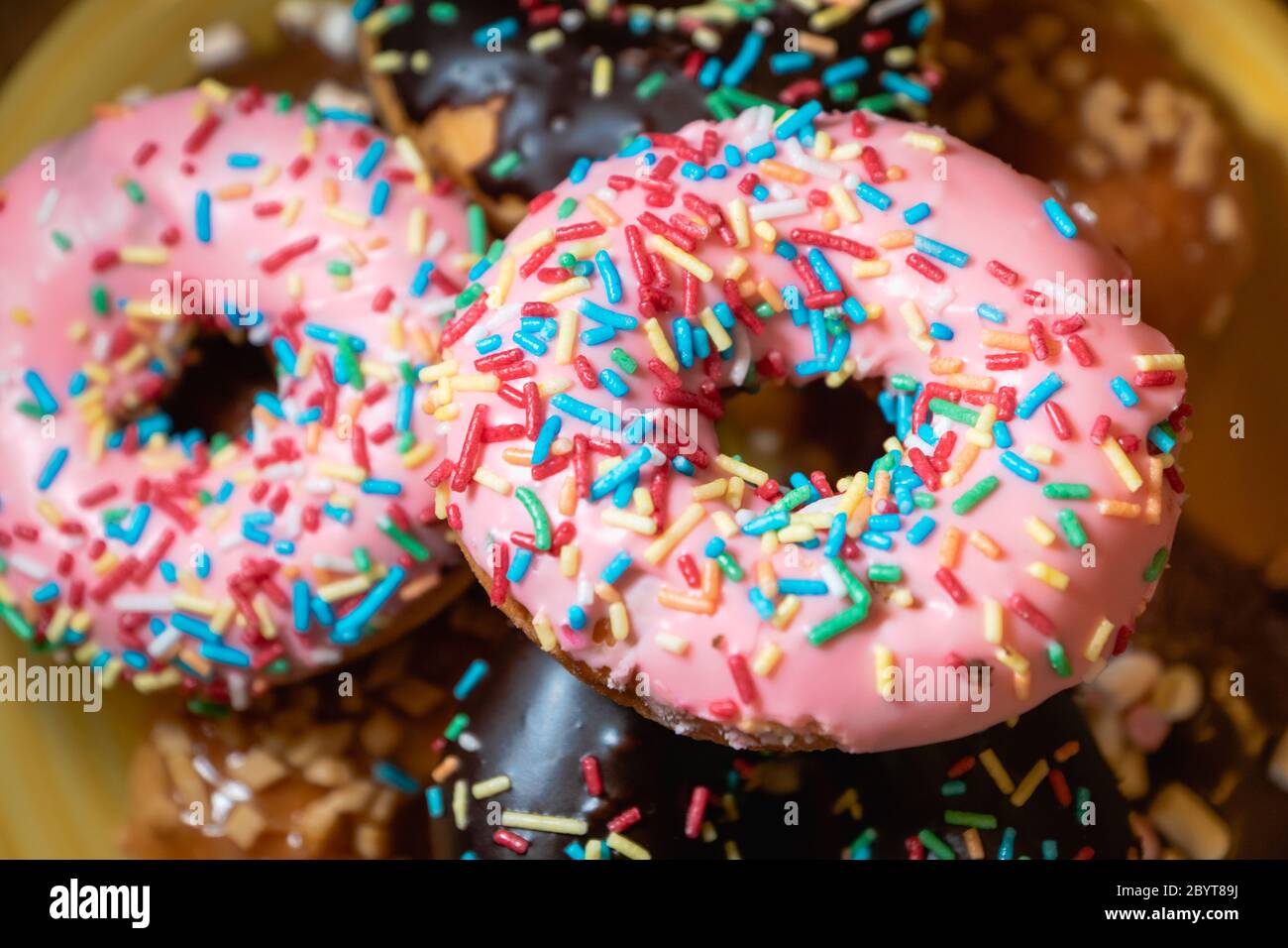 ciambelle, foto in primo piano colorata con messa a fuoco selettiva - ciambelle assortite con cioccolato smerigliato, glassato rosa e spruzzi zuccherati. Foto Stock