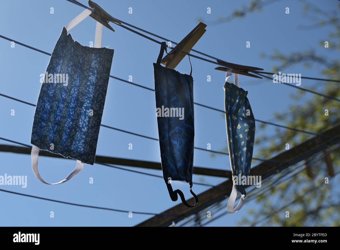 Maschere facciali fatte in casa da una tela dopo il lavaggio per asciugare su una stendibiancheria retroilluminata contro un cielo blu, protezione contro le infezioni durante il decor Foto Stock