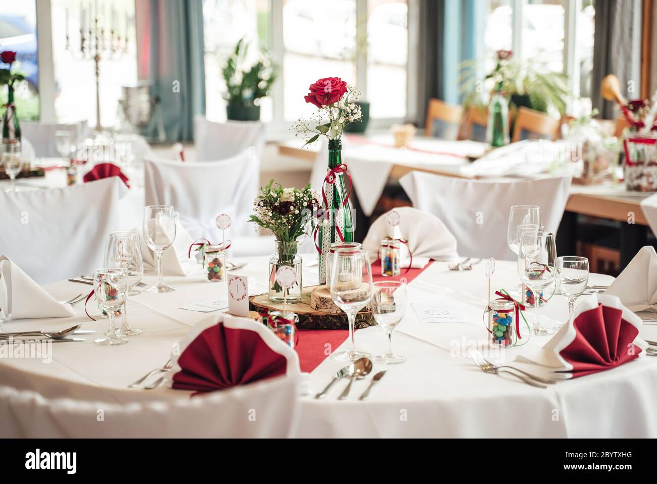 Disposizione di colore bianco decorazione festosa del tavolo. Fiore di rosa rosso in vaso di vetro decorato e disposizione di vetreria. Celebrazione, matrimonio Foto Stock