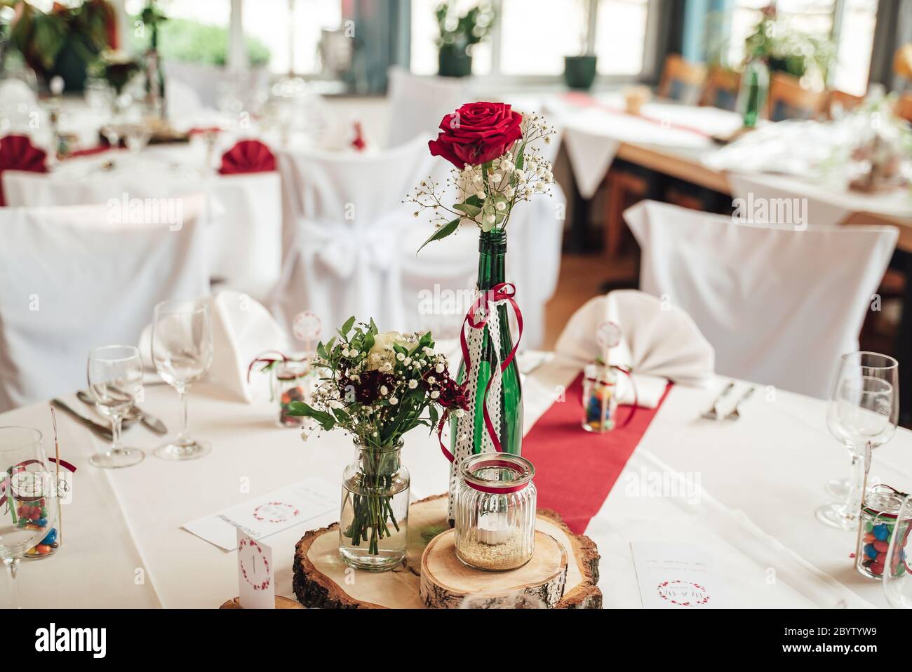Primo piano di fiori di rosa rossa in vaso di vetro decorato e disposizione di vetreria. Decorazione festosa del tavolo. Celebrazione, matrimonio, compleanno Foto Stock