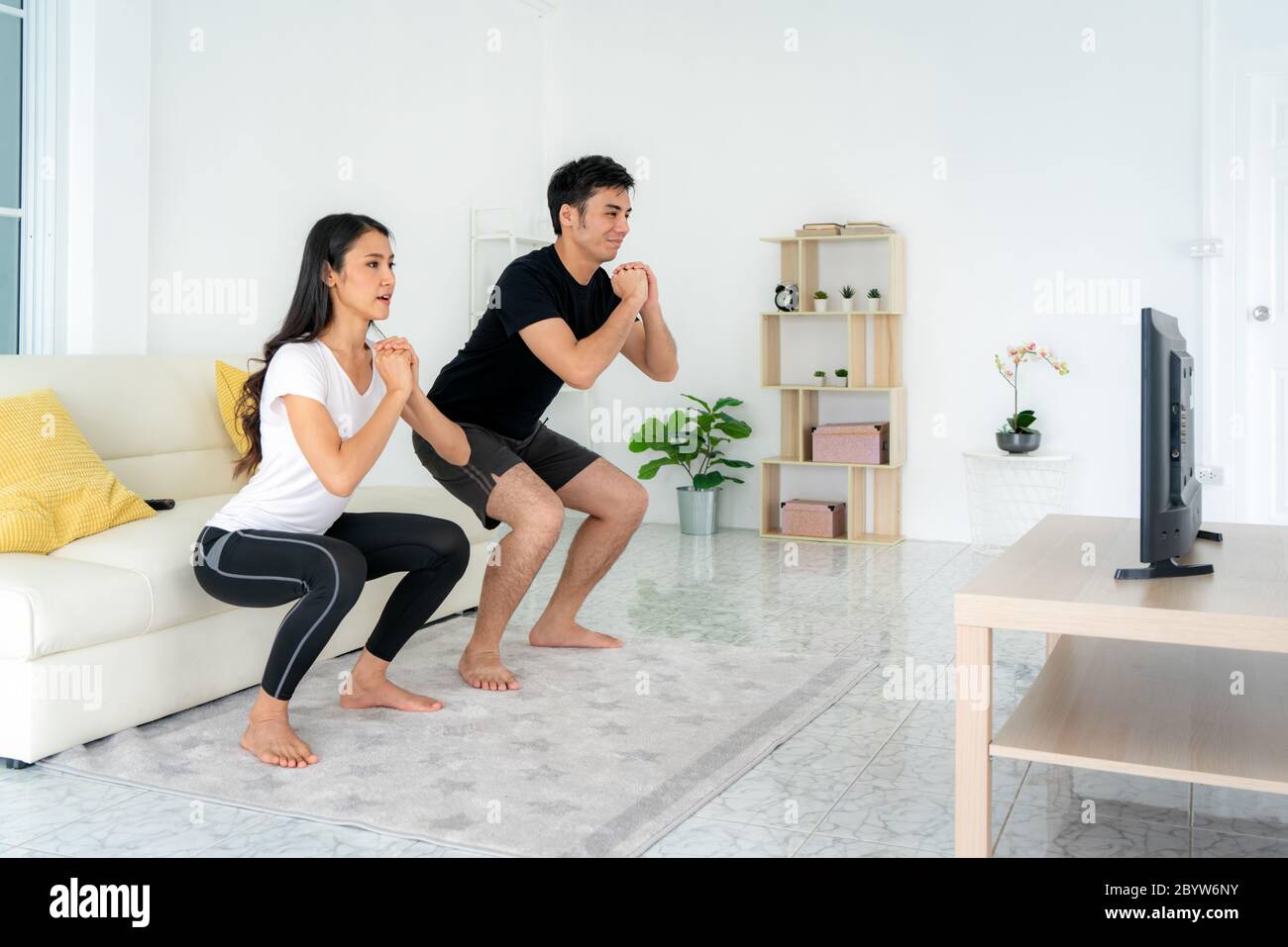 Giovane coppia asiatica che fa squadre che si allenano insieme e guardando la TV a casa, uomo e donna che lavorano insieme in piedi in soggiorno, coppia di fit eseguire Foto Stock