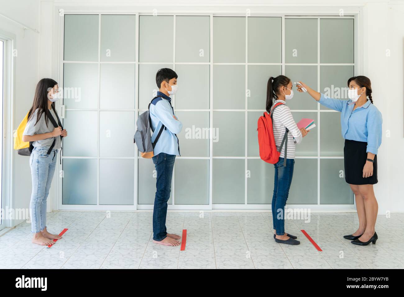 Tre studenti asiatici indossare maschera in piedi distanza di 6 piedi da altre persone mantenere la distanza mentre l'insegnante utilizzando termometro temperatura screening stu Foto Stock
