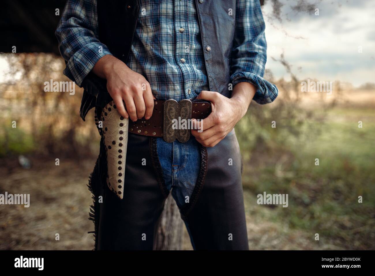 Cowboy in jeans e abbigliamento in pelle con la sua mano sul revolver, texas  ranch sullo sfondo, occidentale. Vintage persona di sesso maschile con la  pistola, wild west lifesty Foto stock -