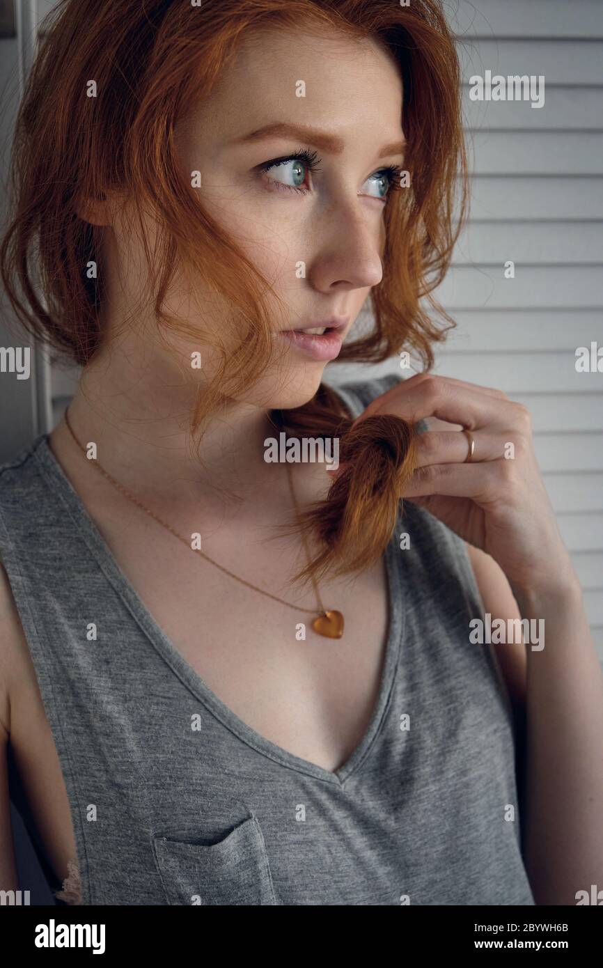 Una ragazza dai capelli rossi si alza a mezzo giro e guarda in lontananza, tenendo la punta di una treccia con la mano. Foto Stock