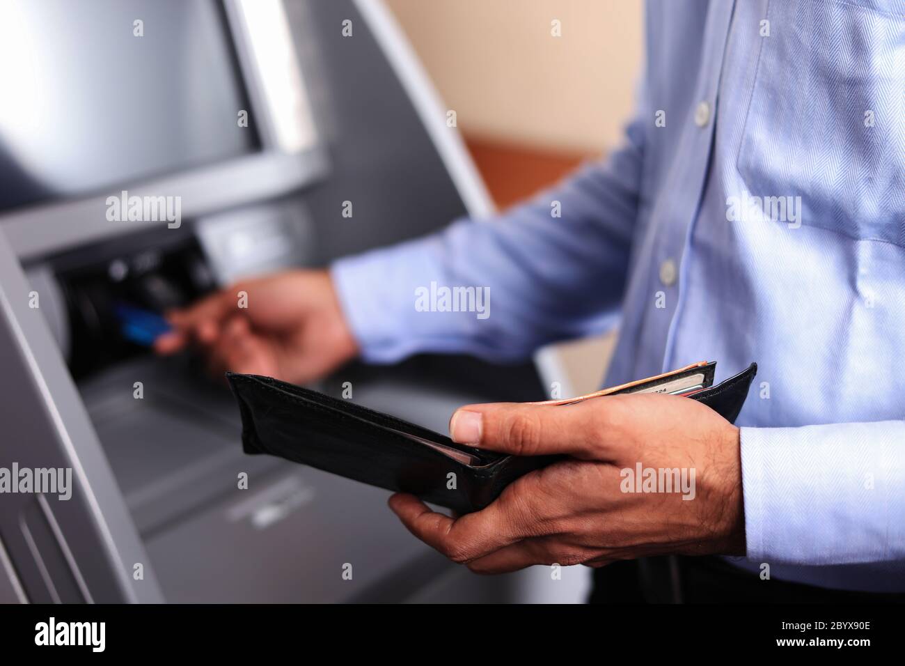 Uomo con un portafoglio nero aperto presso ATM Machine, inserendo una carta di credito. Transazione ATM. Primo piano. Messa a fuoco morbida. Terminale POS. Foto Stock