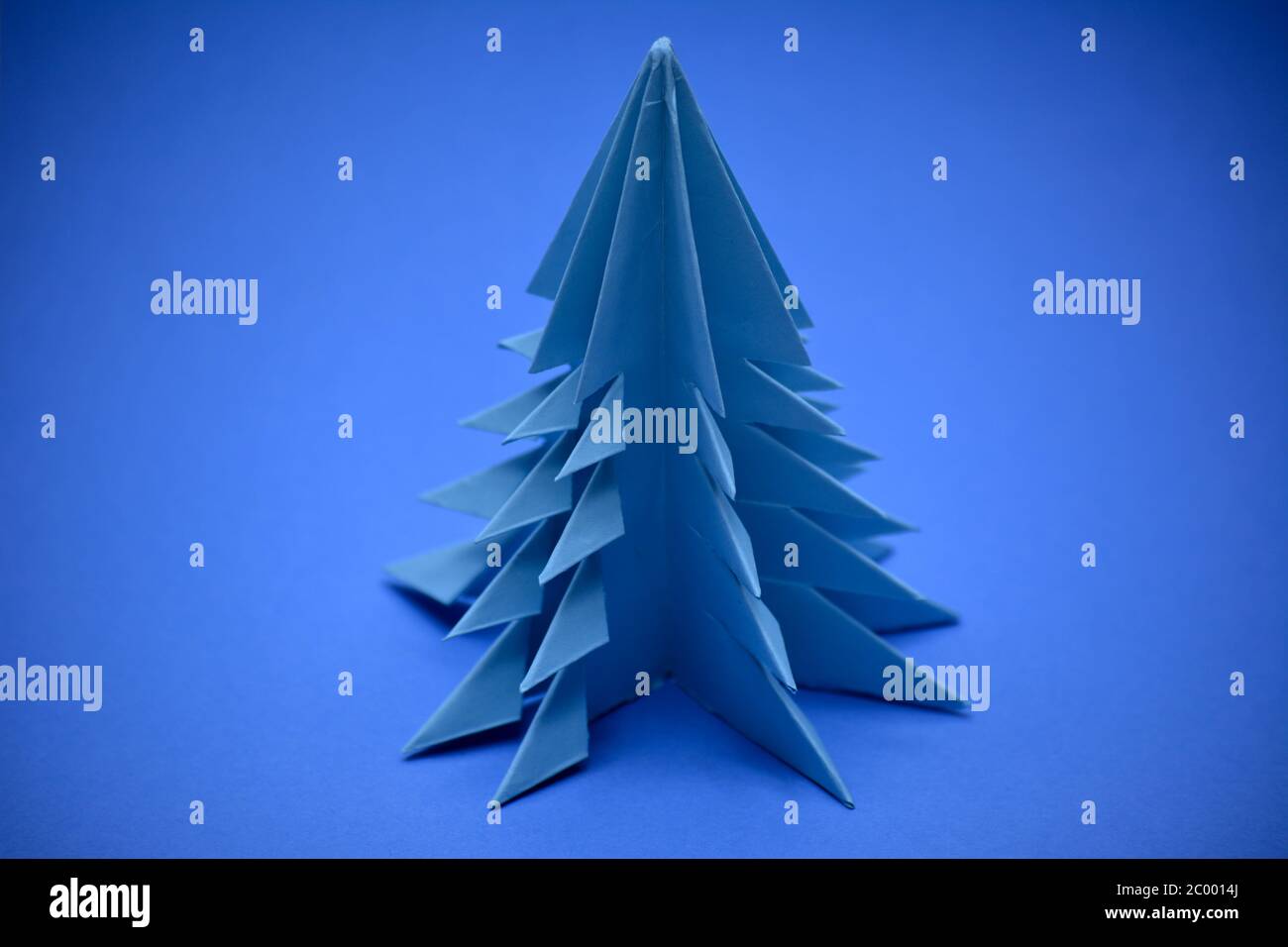Albero di natale blu origami su sfondo blu. Foto Stock
