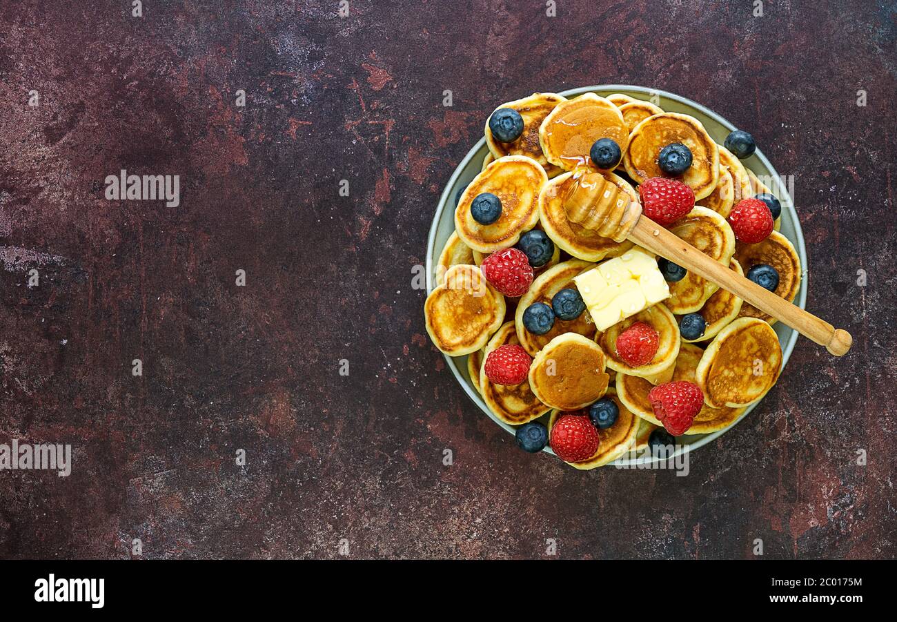 Cibo alla moda - un mucchio di mini pancake cereali in un piatto con burro, frutti di bosco e miele. Foto Stock