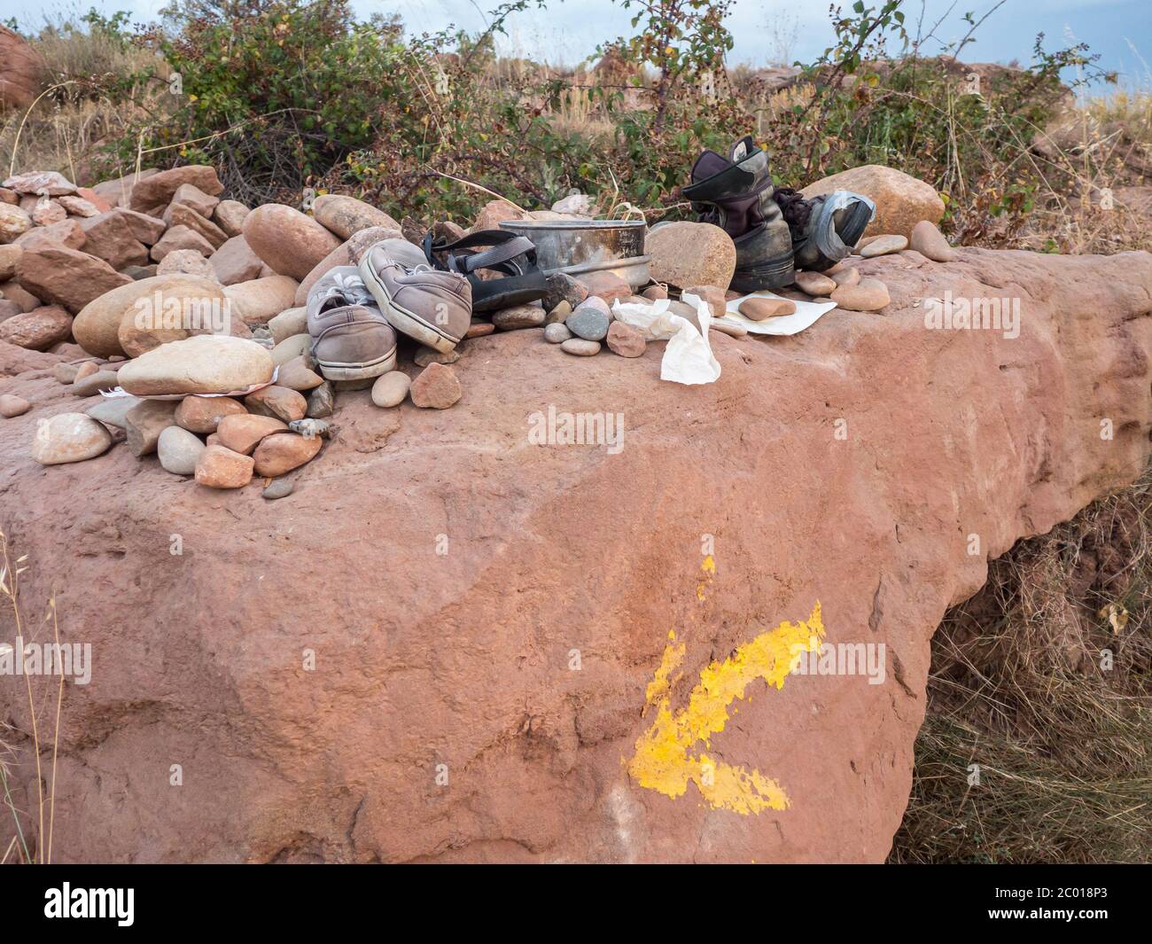 Scarpe vecchie e strappate lasciate dietro insieme con pietre su una roccia con un segno di freccia gialla parzialmente sbiadito da qualche parte in Spagna sulla strada di San James4 Foto Stock