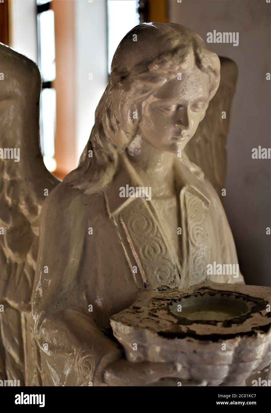 Una statua di un angelo all'ingresso di una chiesa che tiene un bacino che serve come una stoup per l'acqua Santa Foto Stock