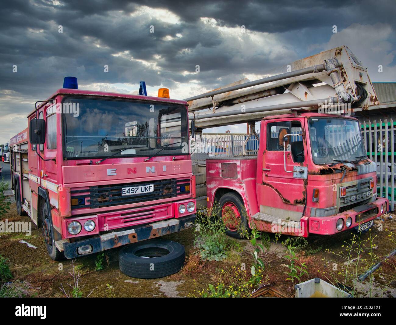 Due abbandonati, arrugginiti, derelict motori di fuoco con vernice sbiadita, uno Dennis e l'altro Dodge, lasciato in un deposito recintato composto. Foto Stock