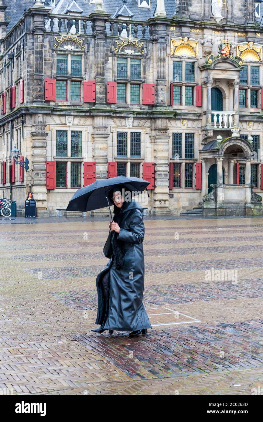 Signora in nero, al riparo dalla pioggia sotto un ombrello in una mattina bagnata a Markt, Delft, Sud Olanda, Paesi Bassi Foto Stock