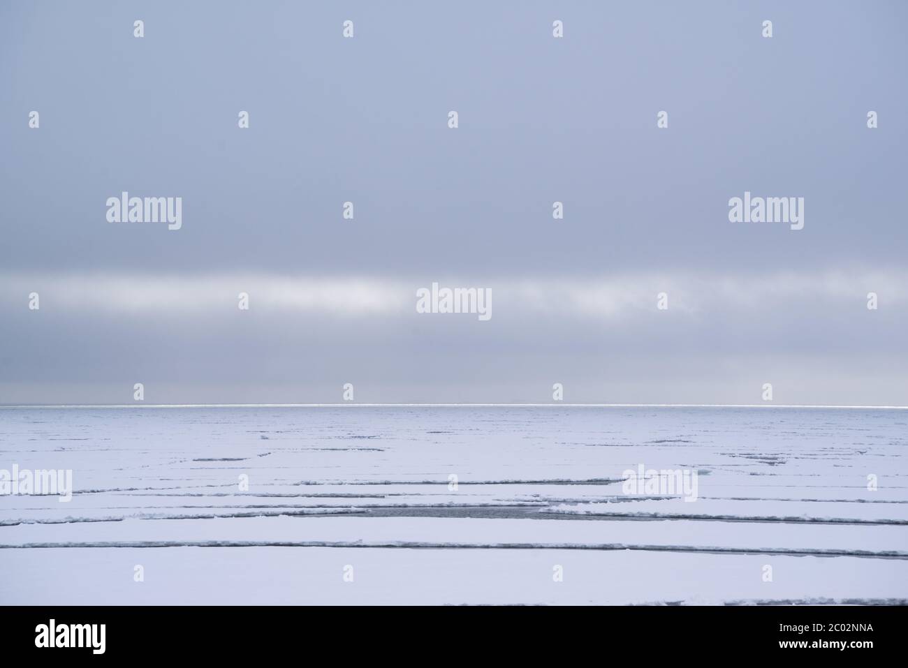 Fiordo artico coperto da ghiaccio marino con un sacco di crepe in esso. Montagne innevate dietro. Foto Stock
