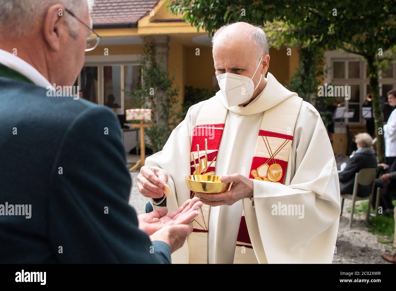 Seehausen am Staffelsee, Germania. 11 Giugno 2020. Padre Raimund Luschin indossa un protettore di bocca e naso e distribuisce le ostie consacrate ai fedeli durante la Santa comunione del festoso servizio del Corpus Domini all'aria aperta di fronte alla chiesa parrocchiale di San Michele. Normalmente ci sarebbe stata la tradizionale processione del Corpus Christi con numerose barche decorate che avrebbero navigato attraverso Staffelsee. La processione del lago è stata annullata quest'anno a causa della pandemia di Corona. Credit: Attualità dal vivo di Matthias Balk/dpa/Alamy Foto Stock