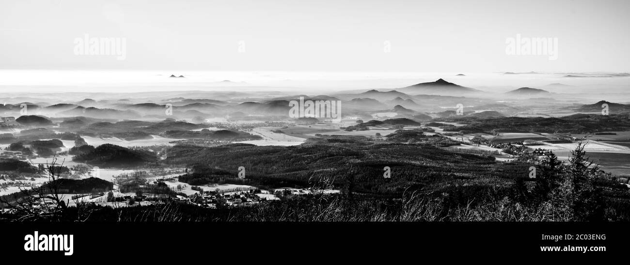 Paesaggio collinare in giornata soleggiata e nebbiosa. Inversione del tempo. Highlands Bohemien centrali, ceco: Ceske stredohori, Repubblica Ceca. Immagine in bianco e nero. Foto Stock