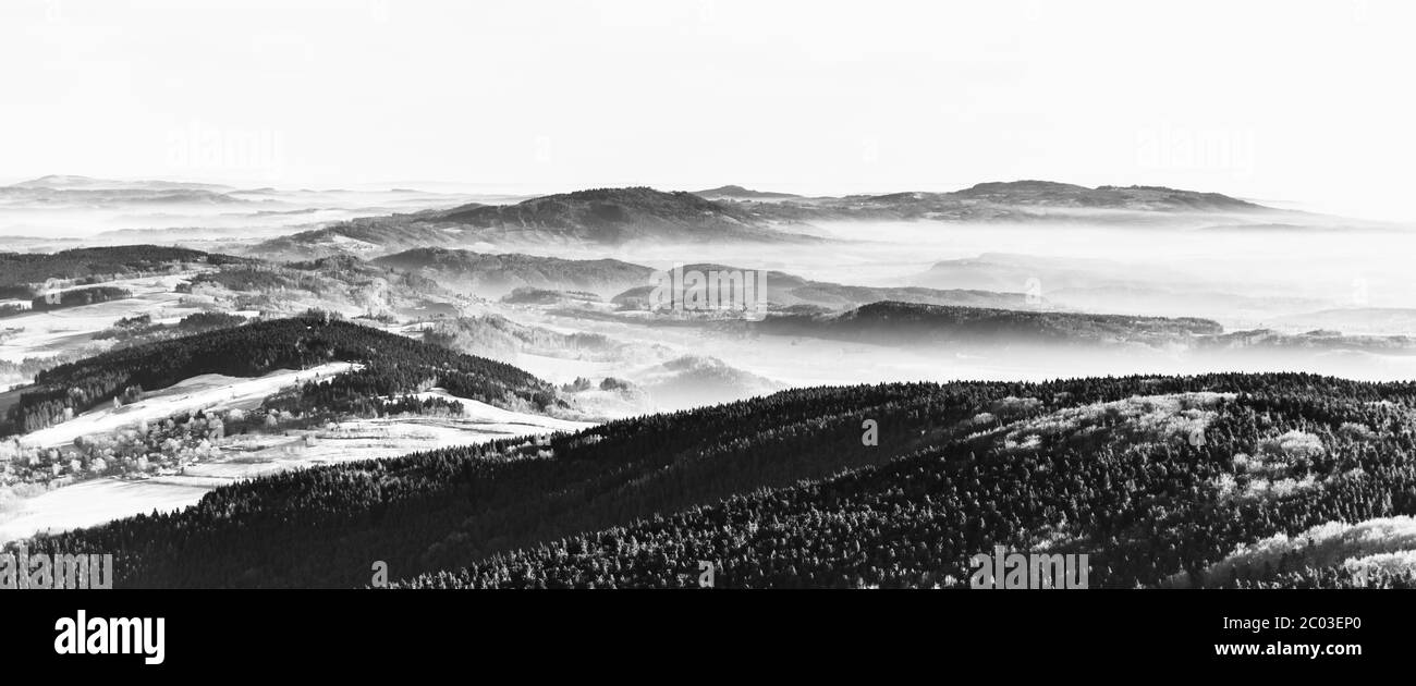 Paesaggio collinare in giornata soleggiata e nebbiosa. Inversione del tempo. Gested - crinale di Kozakov, Repubblica Ceca. Immagine in bianco e nero. Foto Stock