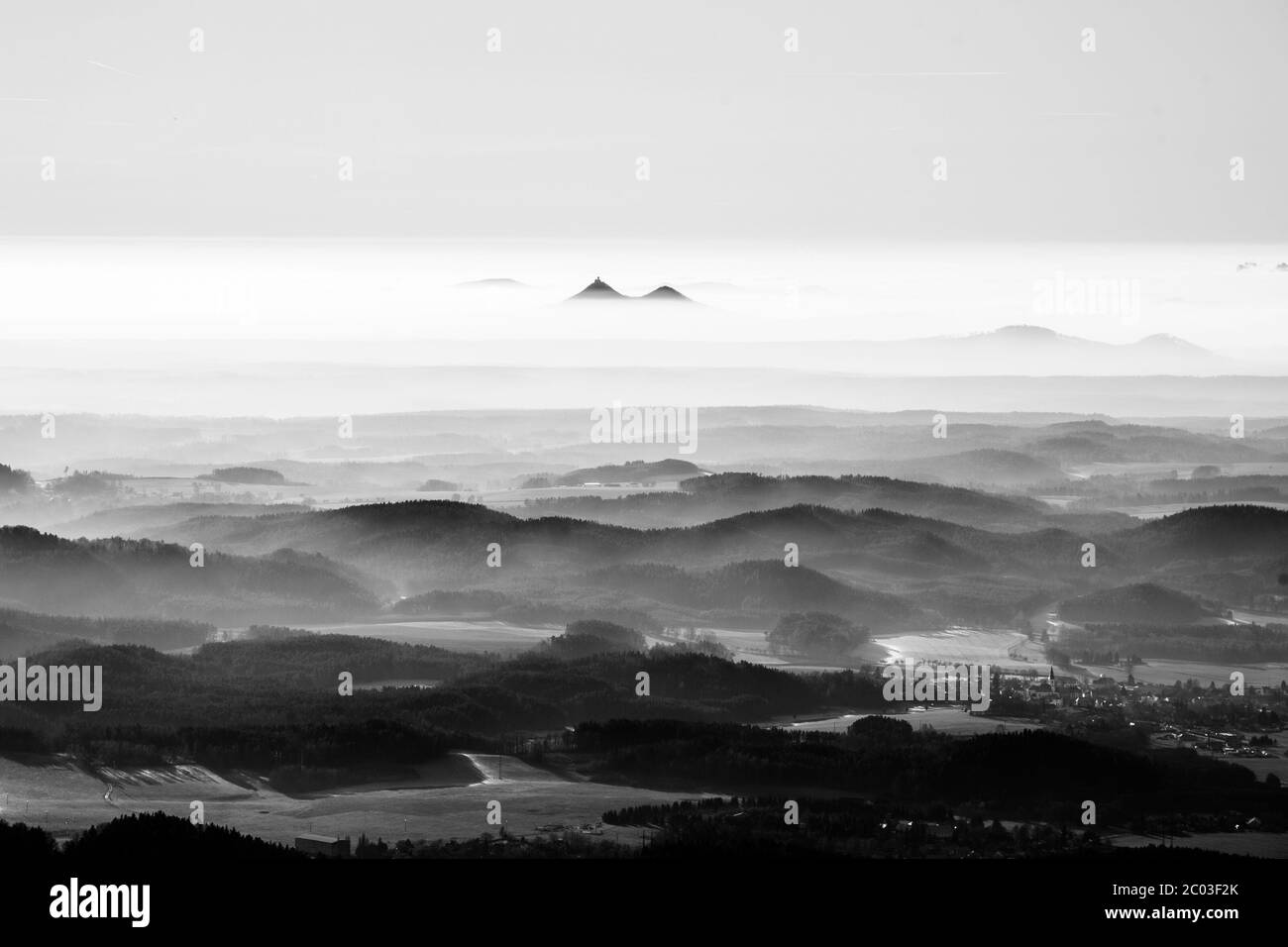 Bezdez gemelle montagne che si innalzano dalla nebbia. Inversione della temperatura meteo, Repubblica Ceca. Immagine in bianco e nero. Foto Stock