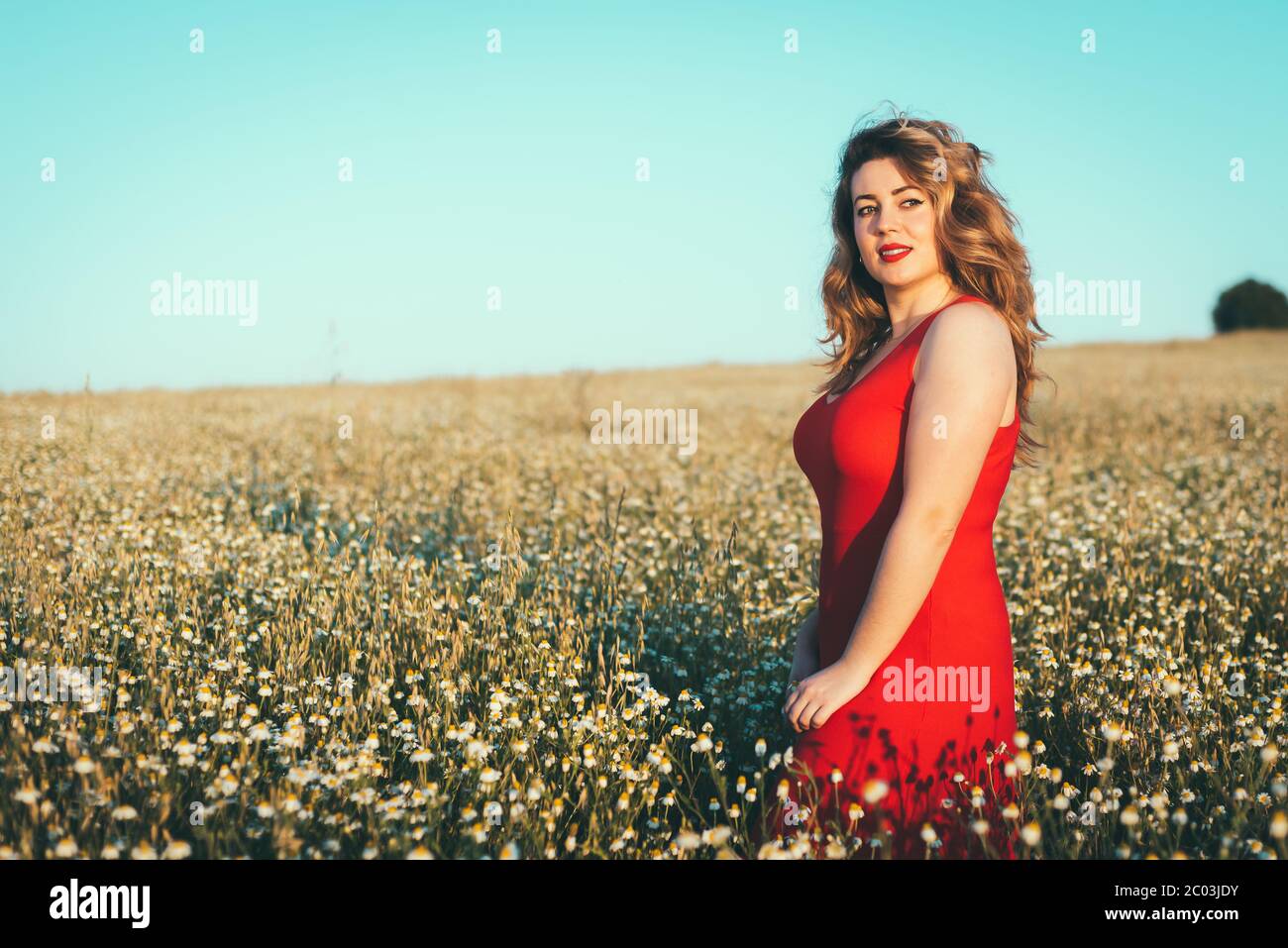 donna in abito rosso che gode di libertà in un campo di margherite Foto Stock