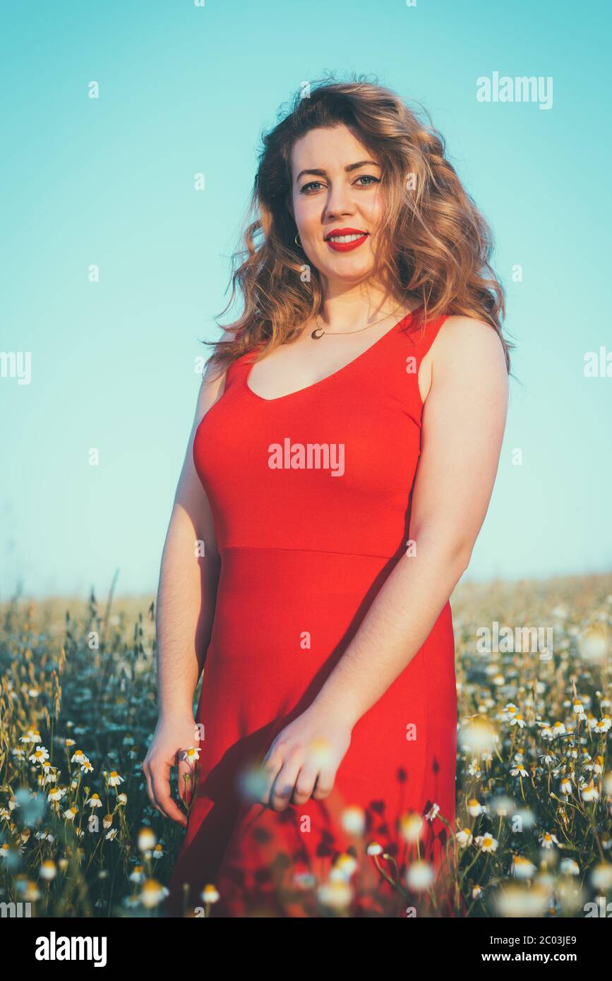 donna in abito rosso che gode di libertà in un campo di margherite Foto Stock