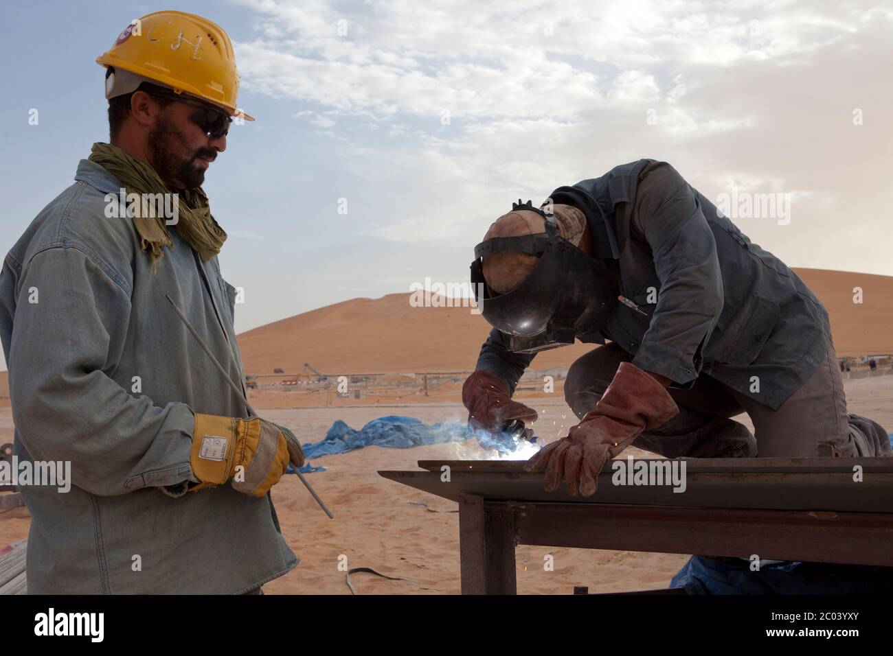 Saldatori in lavoro tagliano lamiera d'acciaio per la costruzione di un serbatoio di olio in un nuovo impianto petrolifero nel deserto del Sahara. Foto Stock