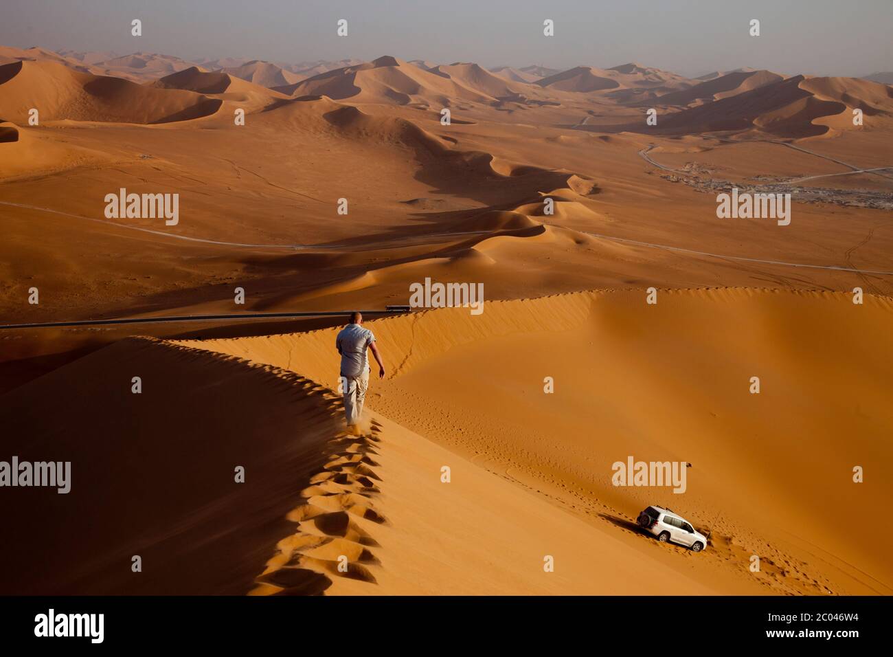 Un lavoratore in un impianto petrolifero in fase di sviluppo nel deserto del Sahara, in Nord Africa, cammina su una duna nel tardo pomeriggio. Foto Stock