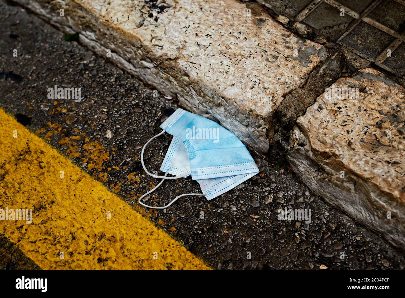 primo piano di una maschera chirurgica blu usata gettata sull'asfalto di una strada cittadina, accanto al marciapiede Foto Stock