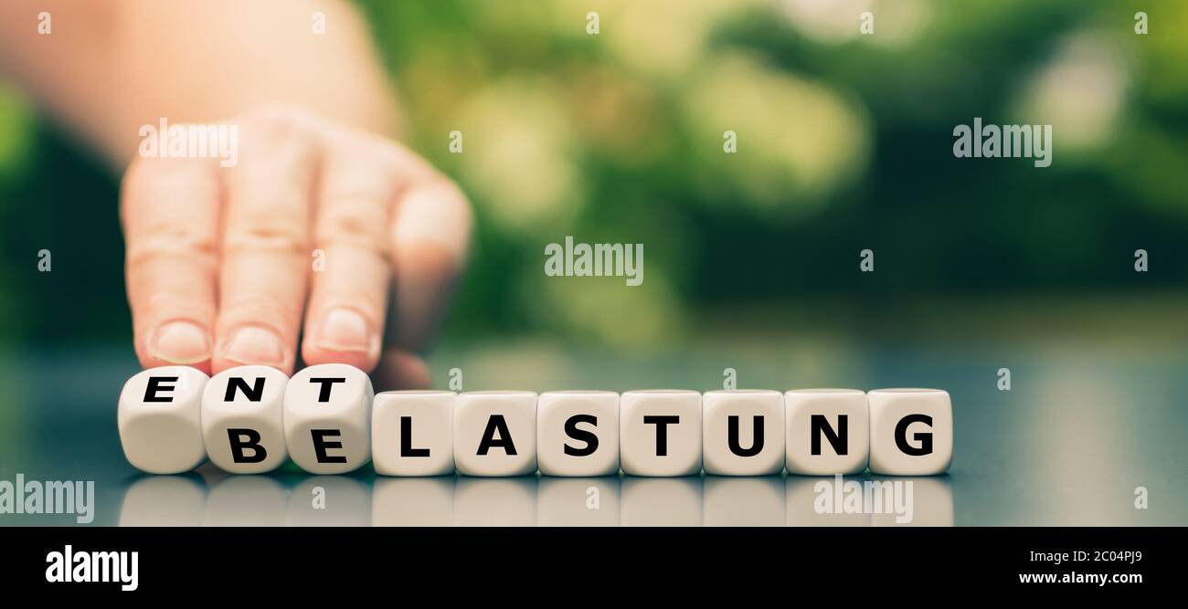 La mano gira i dadi e cambia la parola tedesca 'Belastung' ('carico di lavoro') in 'Entrastung' ('lutto'). Foto Stock