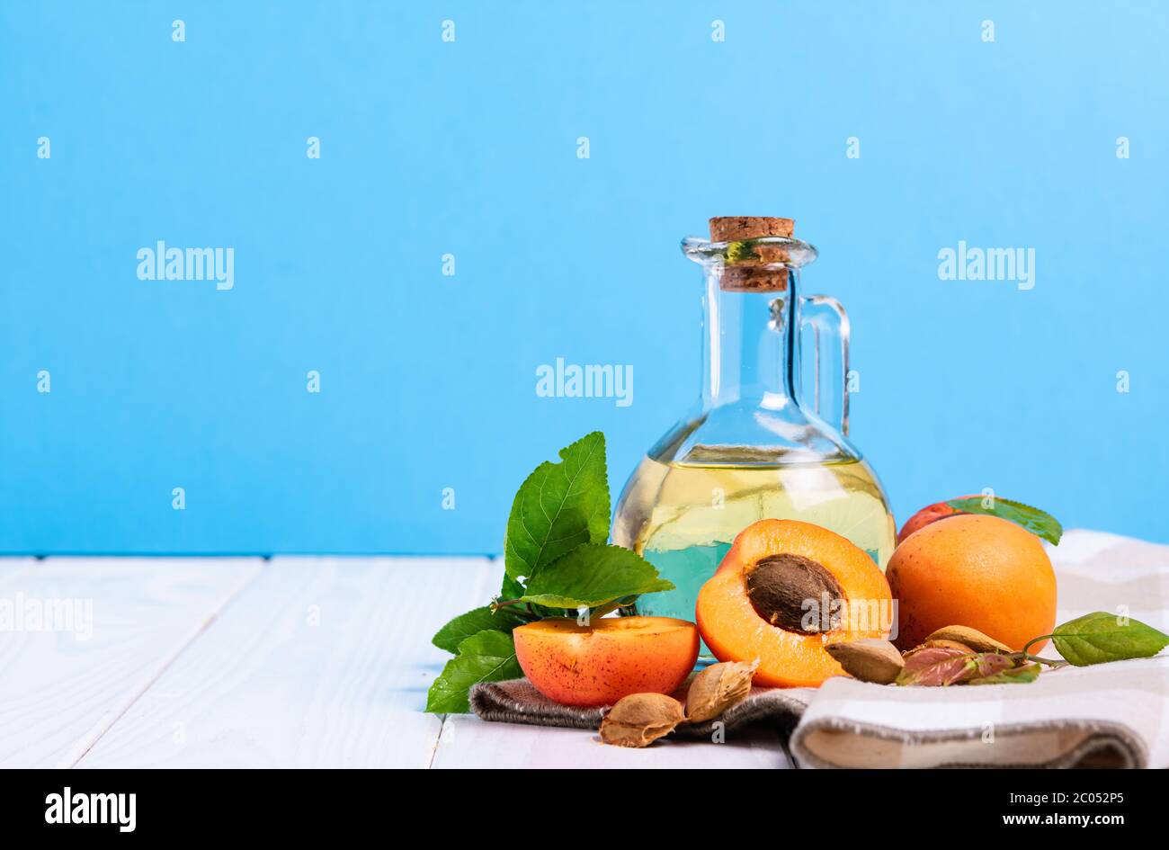composizione, bottiglia con olio di albicocca e semi su un tavolo di legno bianco su fondo blu Foto Stock