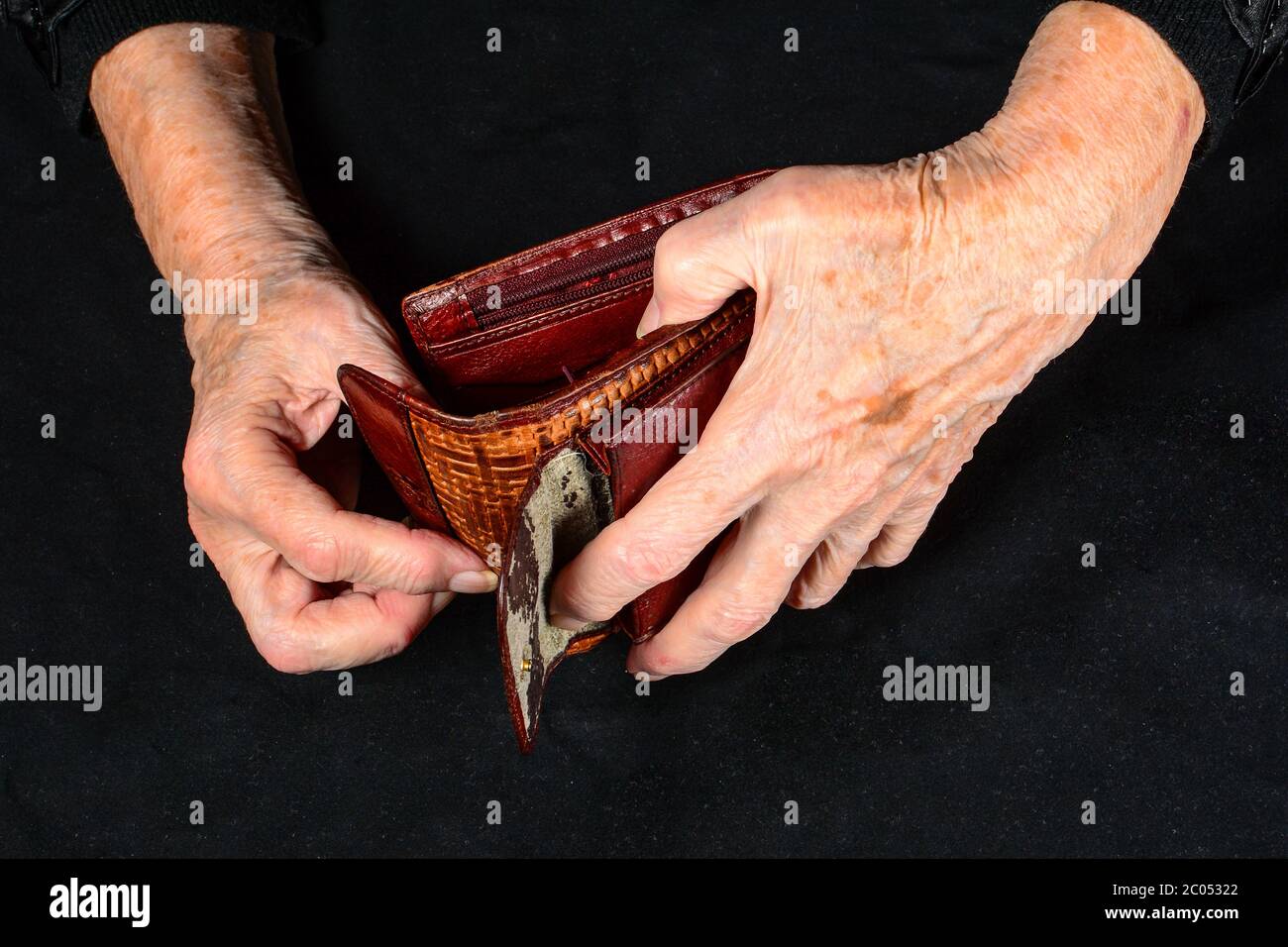 Mani di vecchia donna che cercano di trovare pochi soldi nel vecchio portafoglio shabby. Il concetto di mancanza di denaro in vecchiaia e pensioni di piccola entità. Primo piano al buio Foto Stock