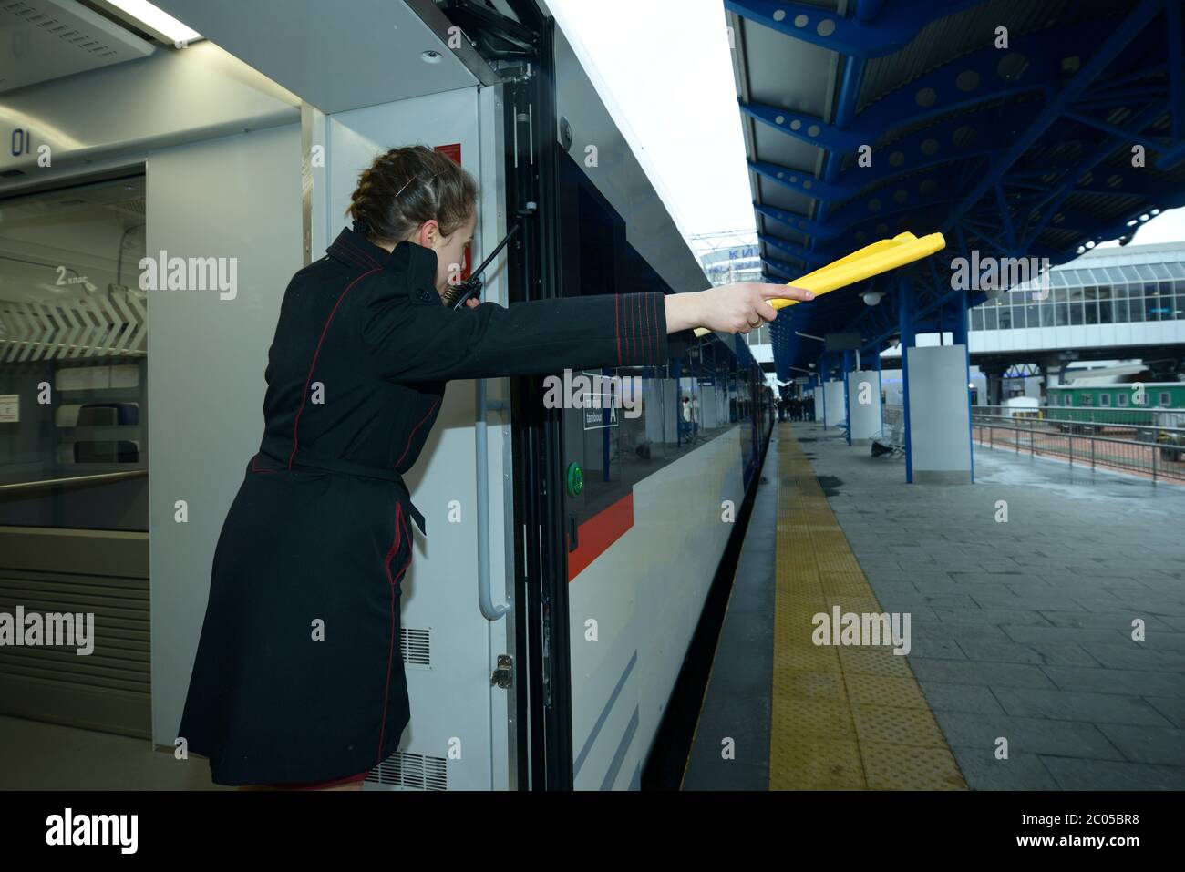 Conduttore ferroviario femminile che parla sul walkie-talkie e segnalazione di partenza del treno passeggeri in piedi sulla piattaforma Foto Stock