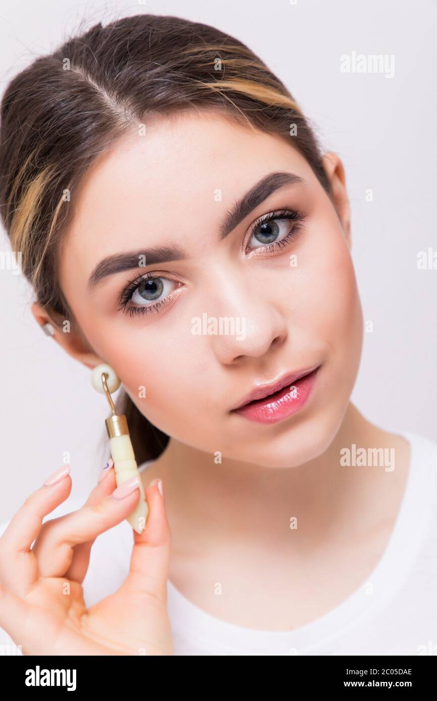 Una giovane bella donna sta facendo un massaggio facciale con un rullo di giada. Massaggiatore a rullo per lisciare le pieghe sul viso. Foto Stock