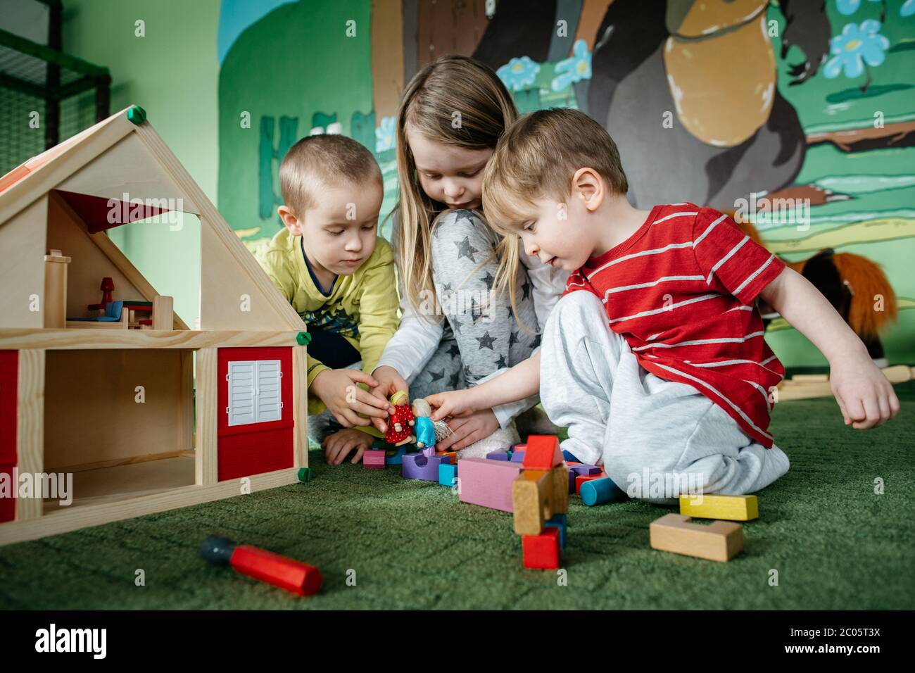 I bambini impegnati giocano con una casa di bambola in legno e piovano persone in un centro giochi Foto Stock