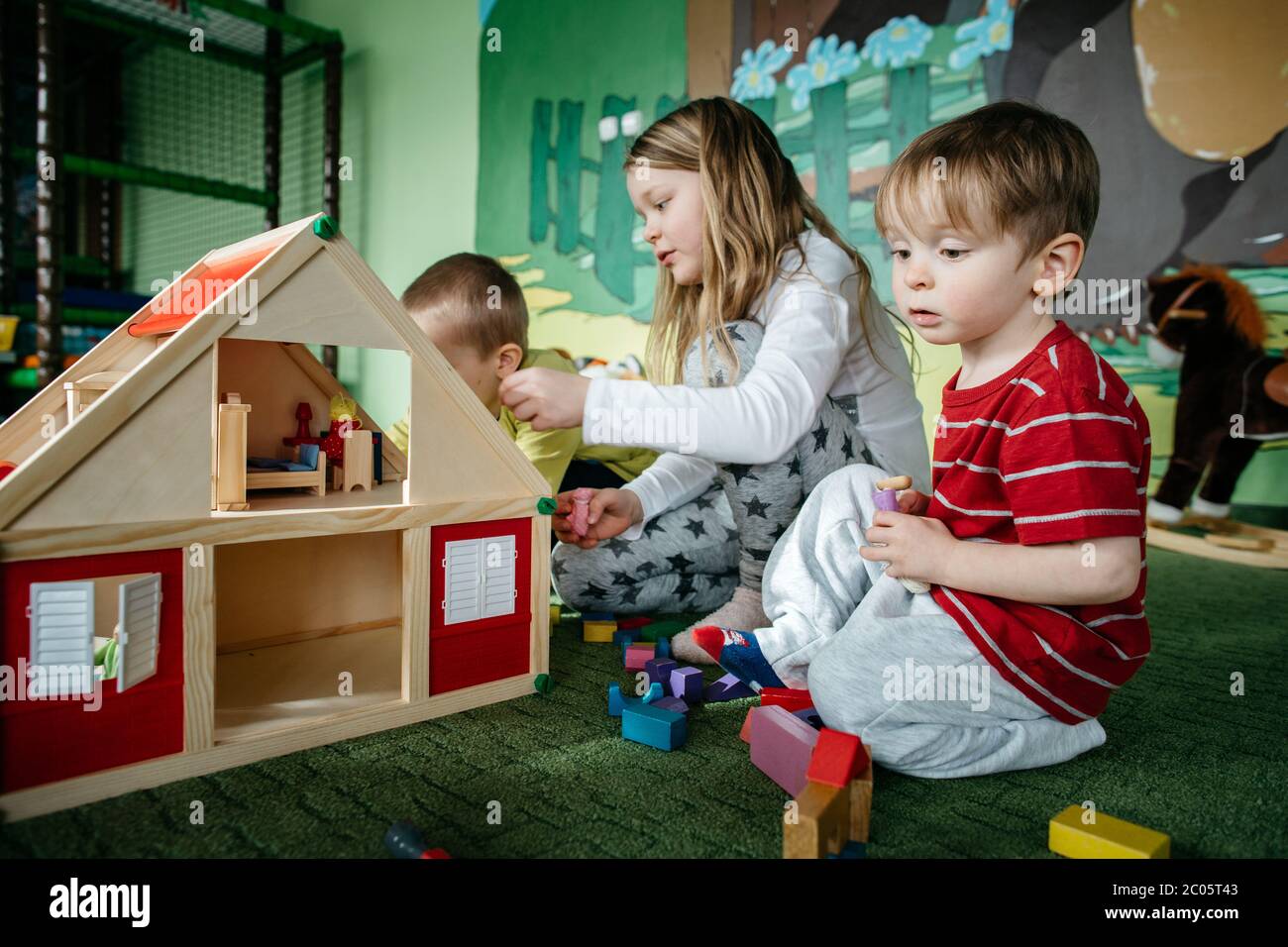 I bambini giocano con una casa di bambola in legno e alloggiano persone in un centro giochi Foto Stock