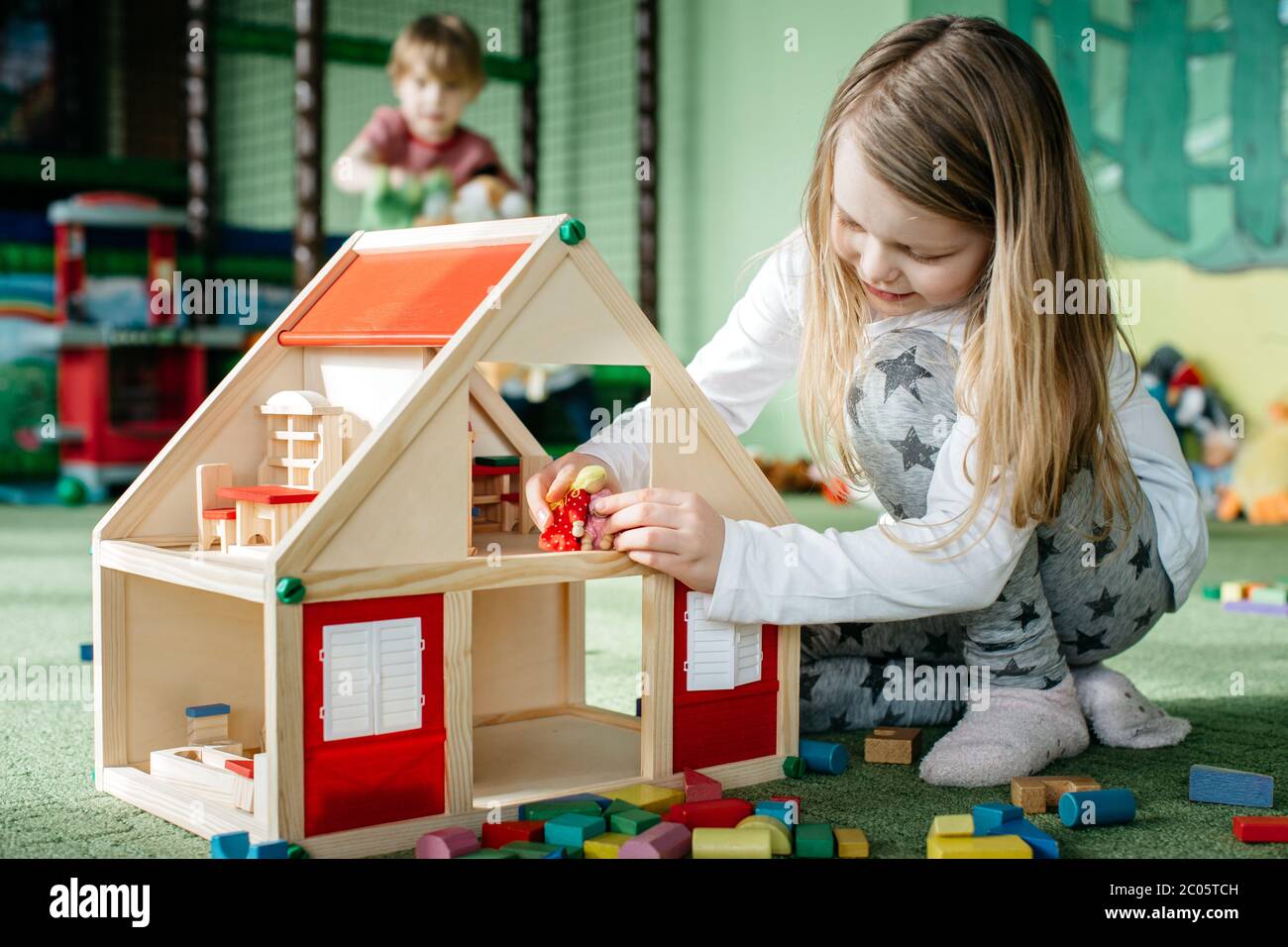 Ragazza che gioca con una casa di bambola in legno e persone di spina in un parco giochi al coperto Foto Stock