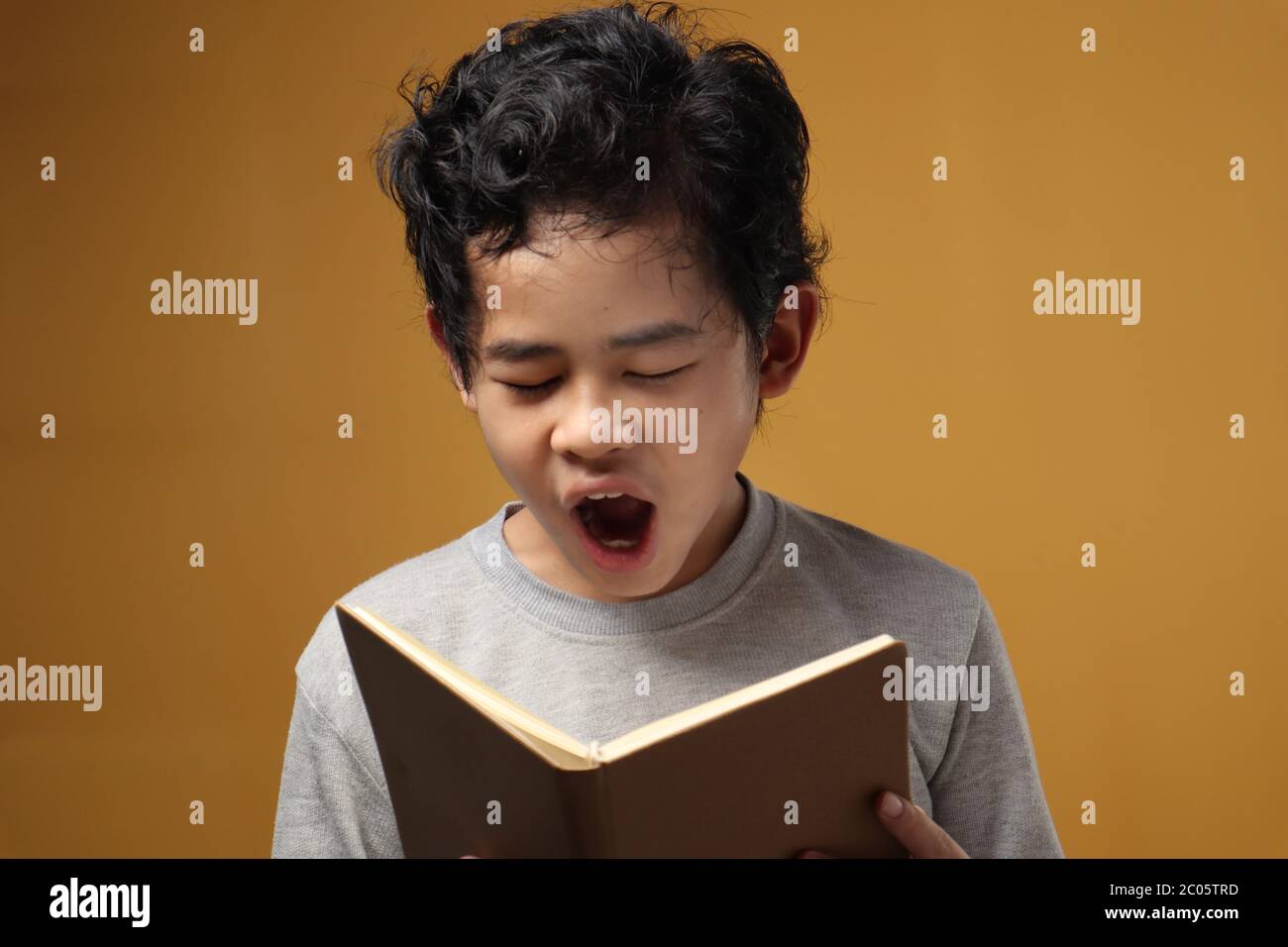 Ritratto di giovane studente asiatico ragazzo stanco sonnolento e sbadigli durante la lettura di un libro, studente stanco quando studia duro, su sfondo giallo Foto Stock