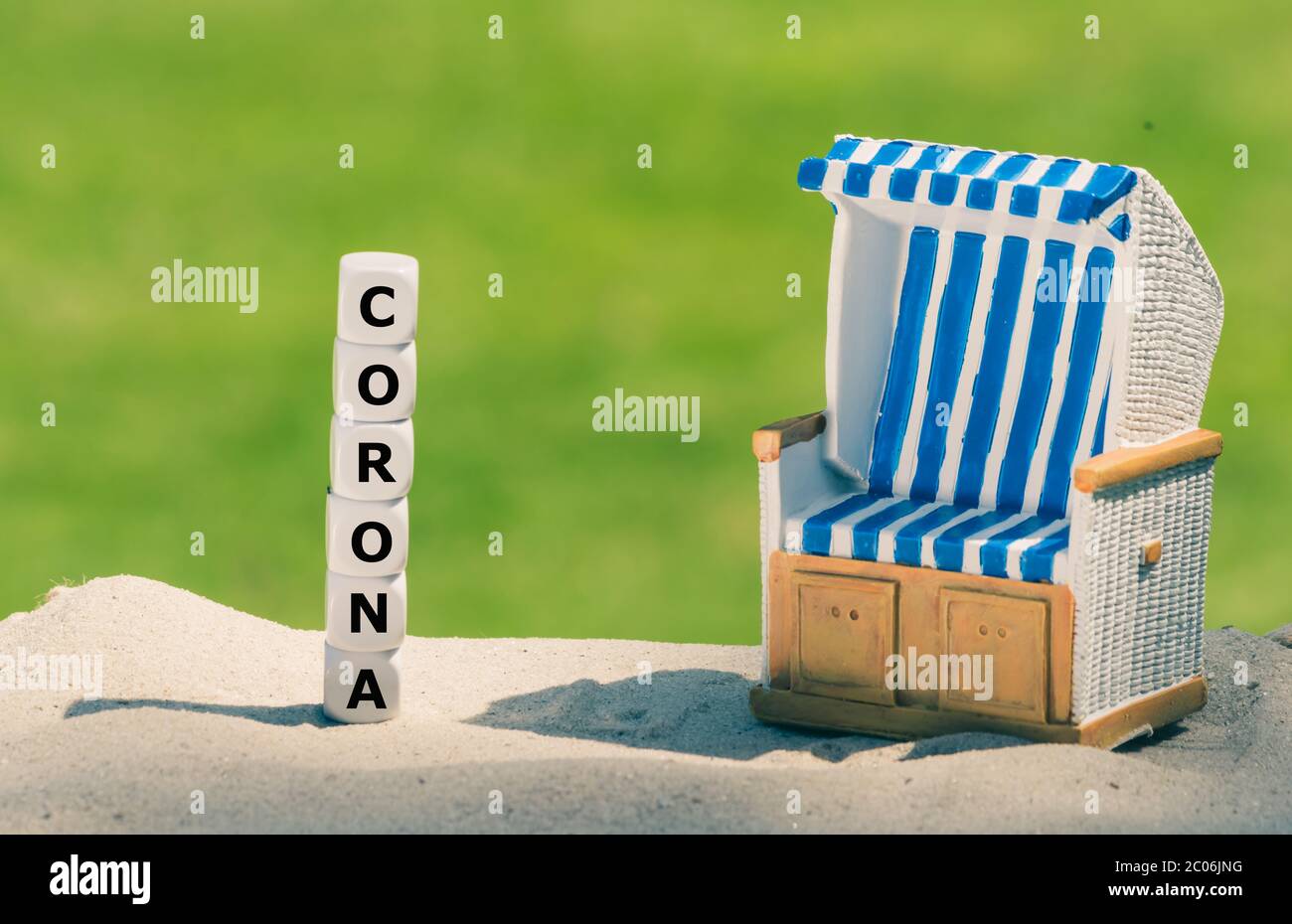 Simbolo per le vacanze durante la crisi della corona. I dadi formano la parola 'corona' accanto ad una sedia da spiaggia. Foto Stock