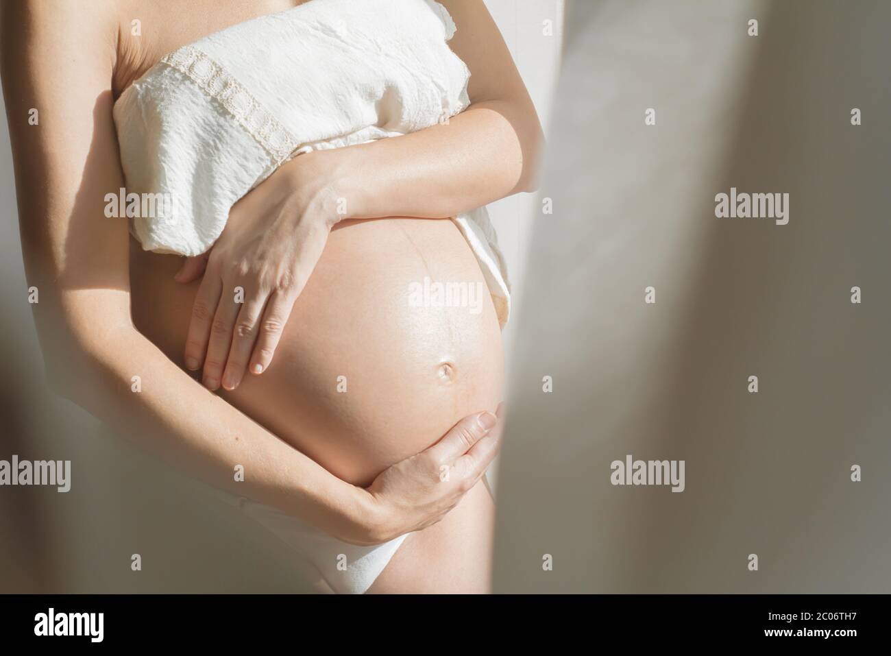 le mani calde e gentili carezzano il bel ventre incinta, il concetto, le lenzuola artistiche e il tessuto bianco carezza donna intimità Foto Stock