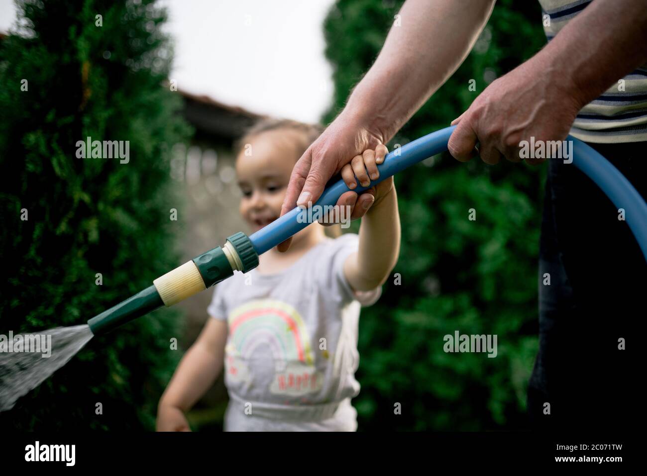 Piccola ragazza che innaffia il giardino con il nonno. Foto Stock
