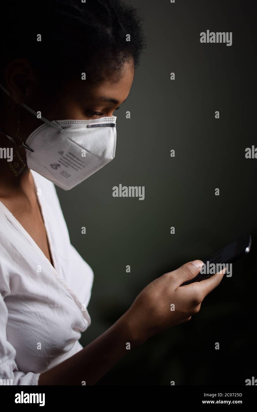 Giovane donna latina che indossa una maschera facciale e utilizza uno smartphone Foto Stock