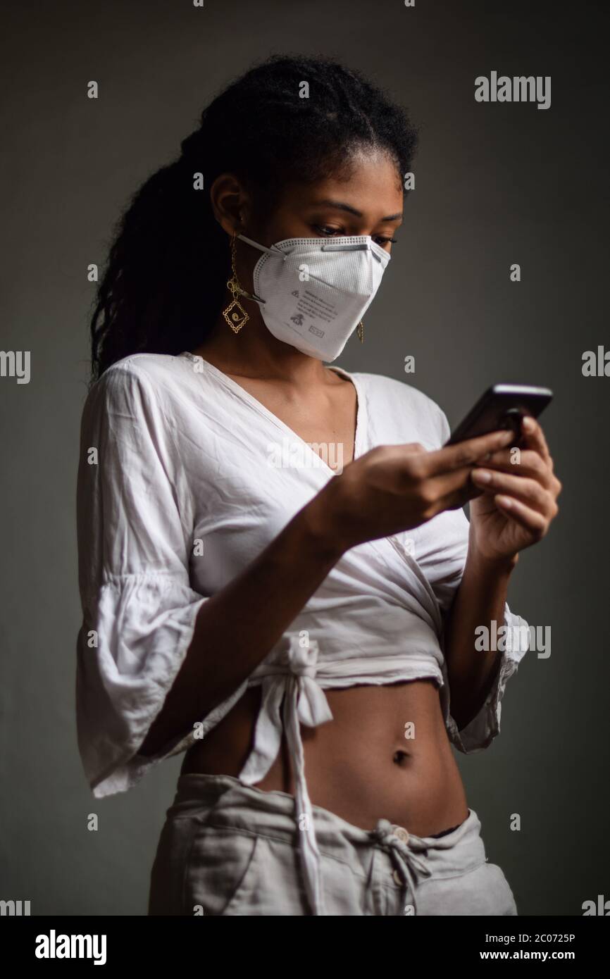 Giovane donna latina che indossa una maschera facciale e utilizza uno smartphone Foto Stock