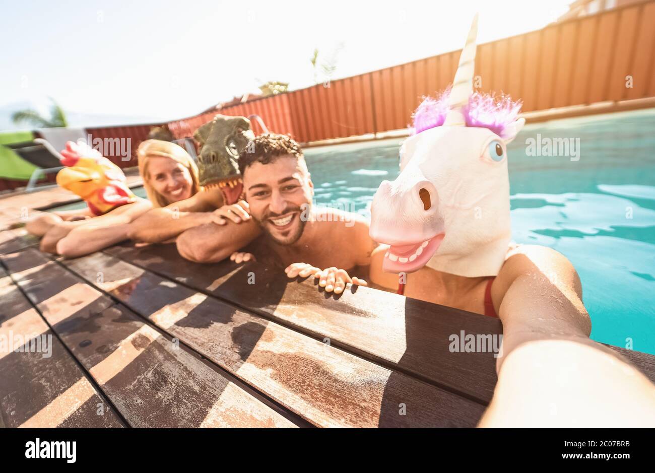 Amici pazzi selfie fare festa in piscina indossare una maschera bizzarra - giovani che si divertono a celebrare l'estate in un esclusivo resort tropicale Foto Stock