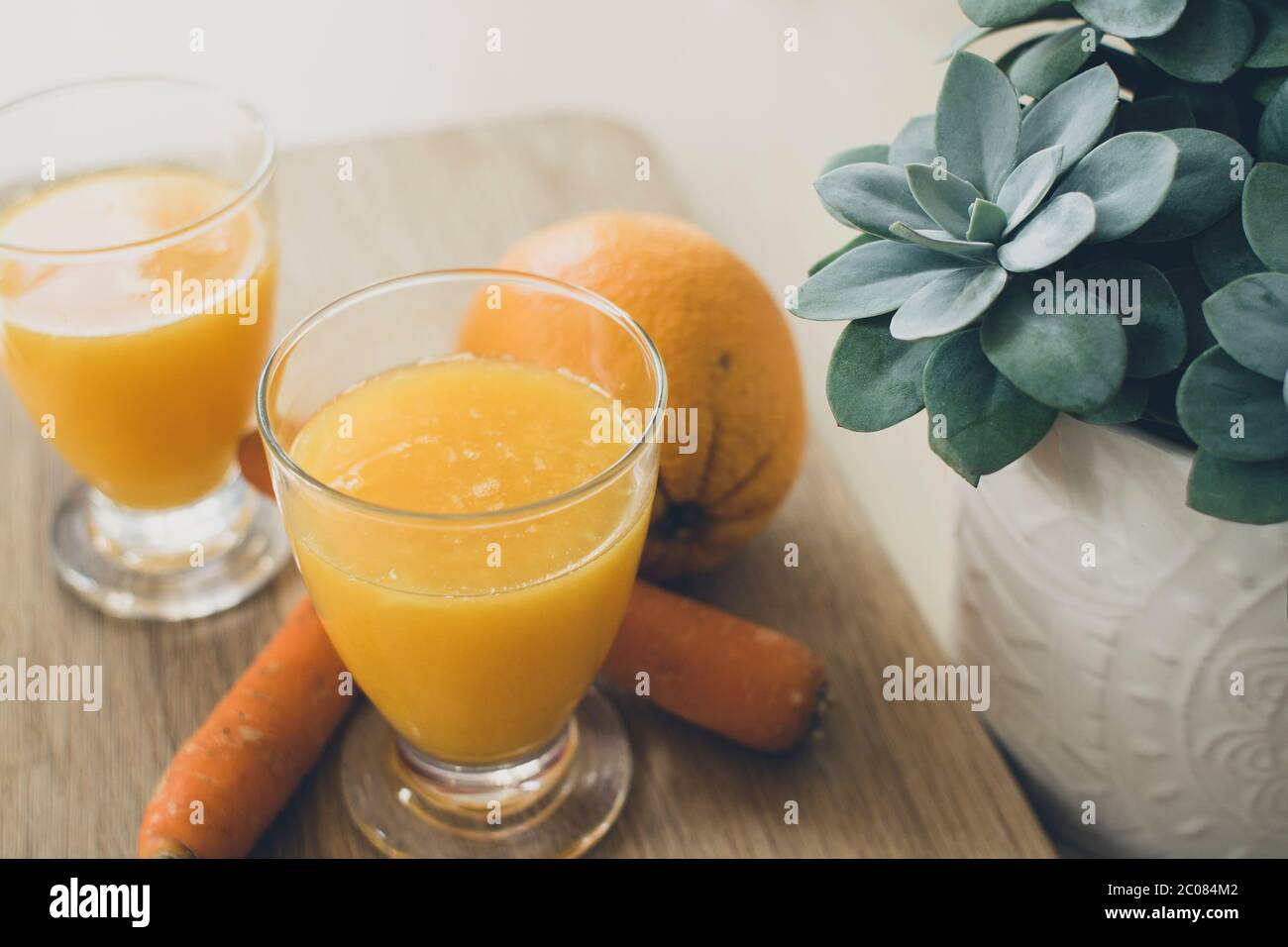 Colazione salutare con succo d'arancia, oragnge, carote e una pianta su legno Foto Stock