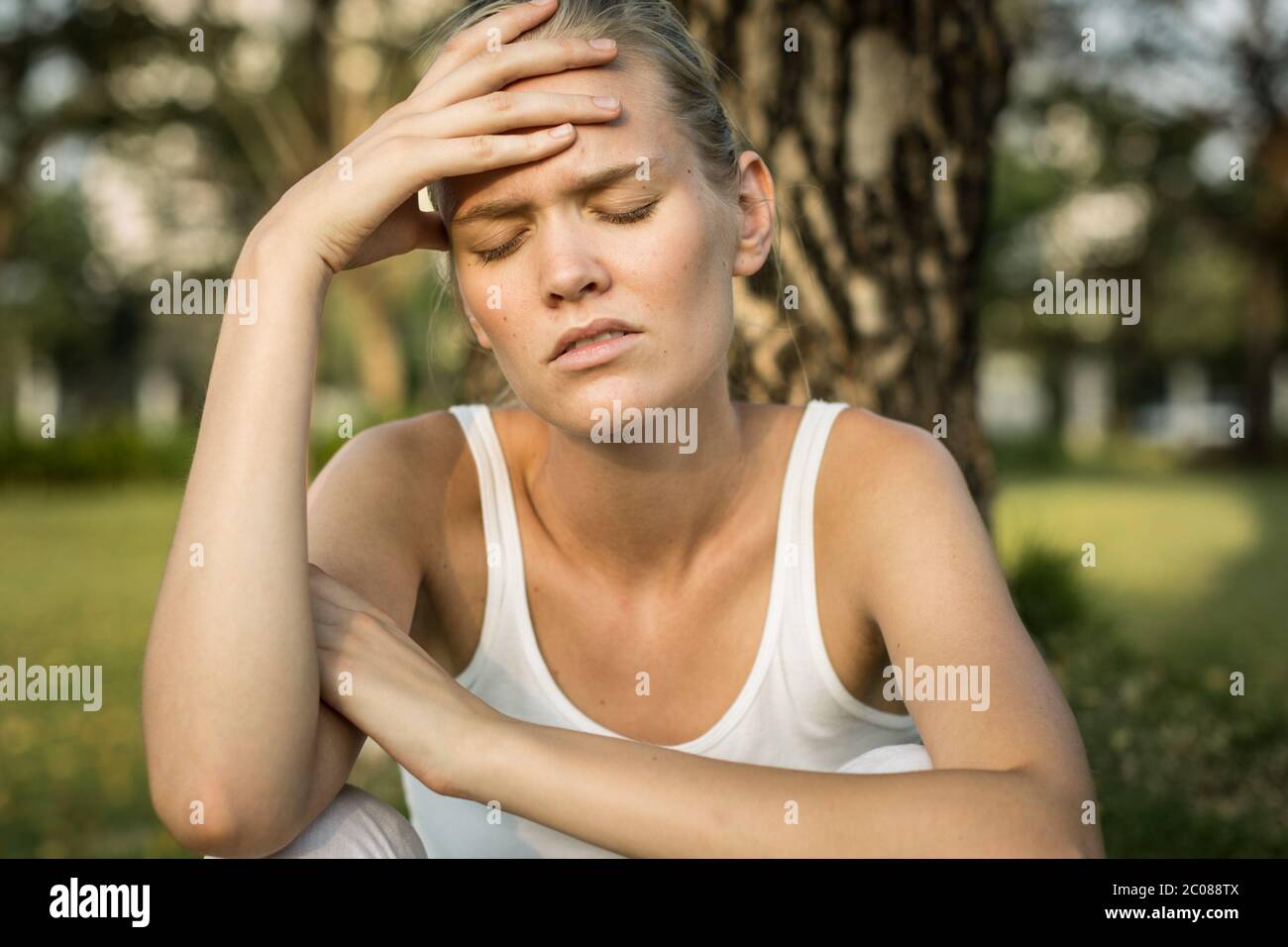 Una ragazza stanca con mal di testa che cerca di affrontare all'esterno del parco Foto Stock