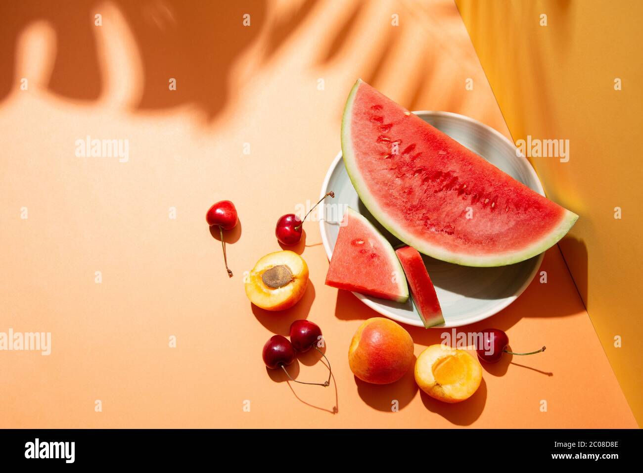 Composizione di frutta estiva alla moda con foglie tropicali ombreggiate su un set arancione e giallo. Spazio di copia Foto Stock