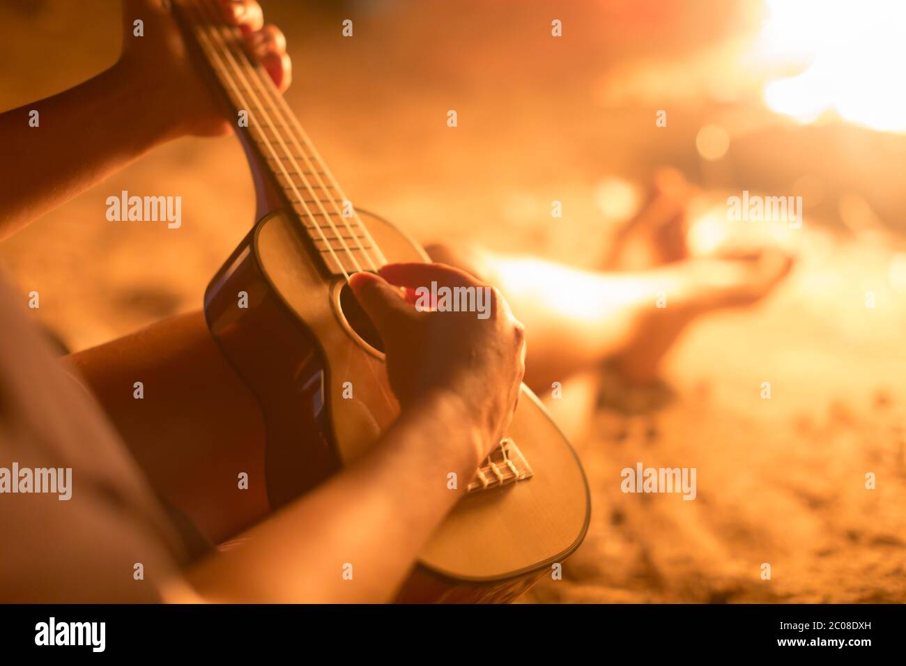 Una musicista femminile che suona la chitarra fuori, seduto accanto ad un fuoco. Relax. Foto Stock
